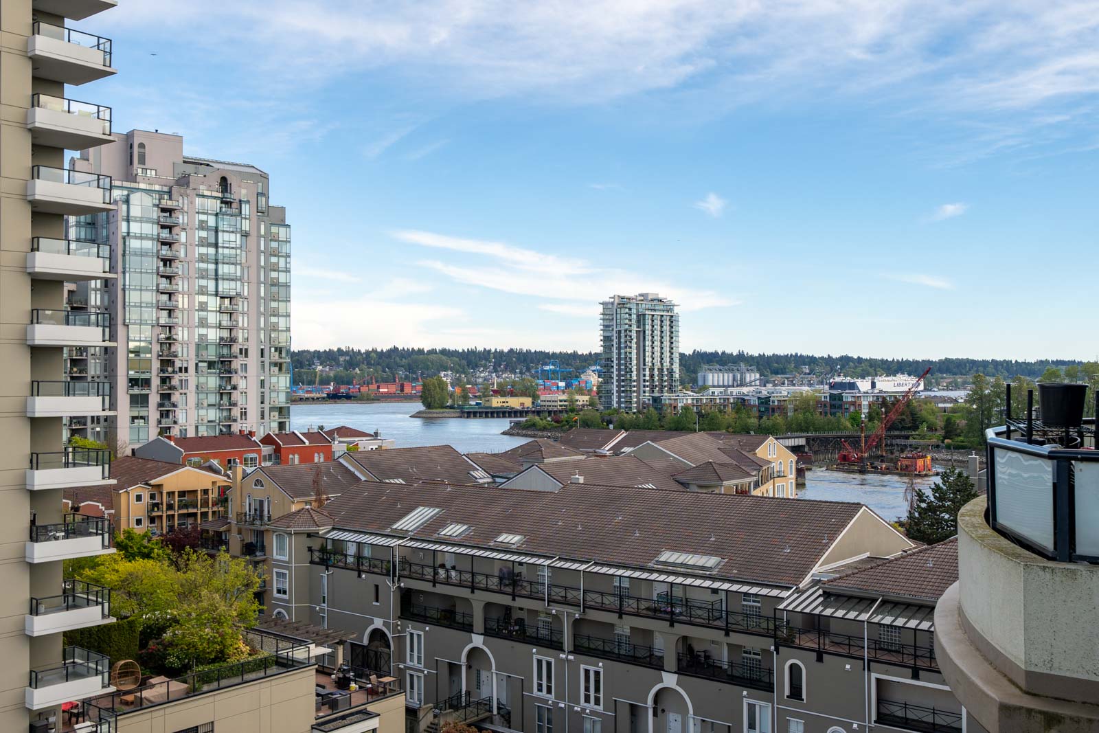 View of mid-rise apartment buildings, a river, and a cluster of colorful low-rise buildings with trees and blue sky in the background.