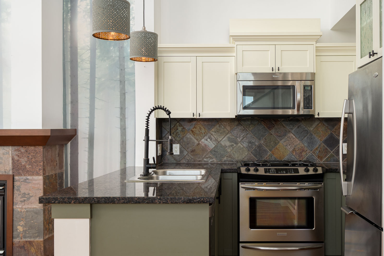 Modern kitchen with slate tile backsplash, stainless steel appliances, granite countertop, double oven, built-in microwave, and pendant lighting above a sink with a black faucet.