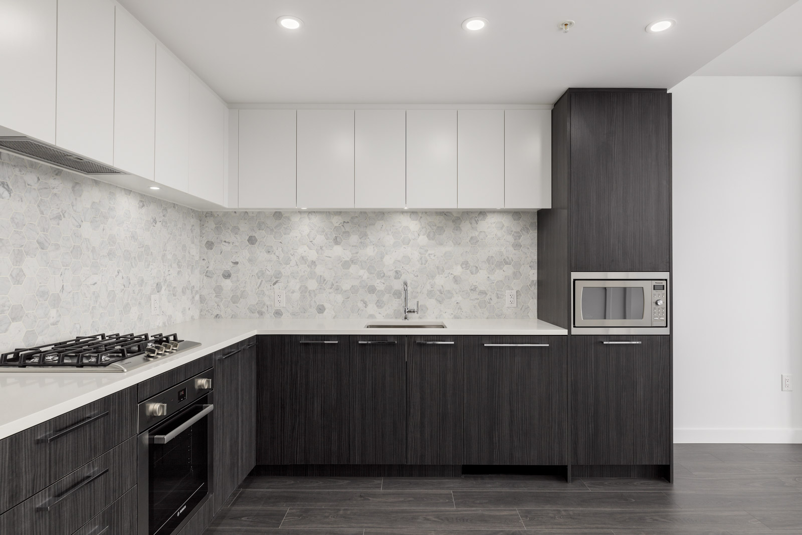 Modern kitchen with white upper cabinets, dark lower cabinets, a built-in oven, gas cooktop, microwave, and hexagonal tile backsplash.