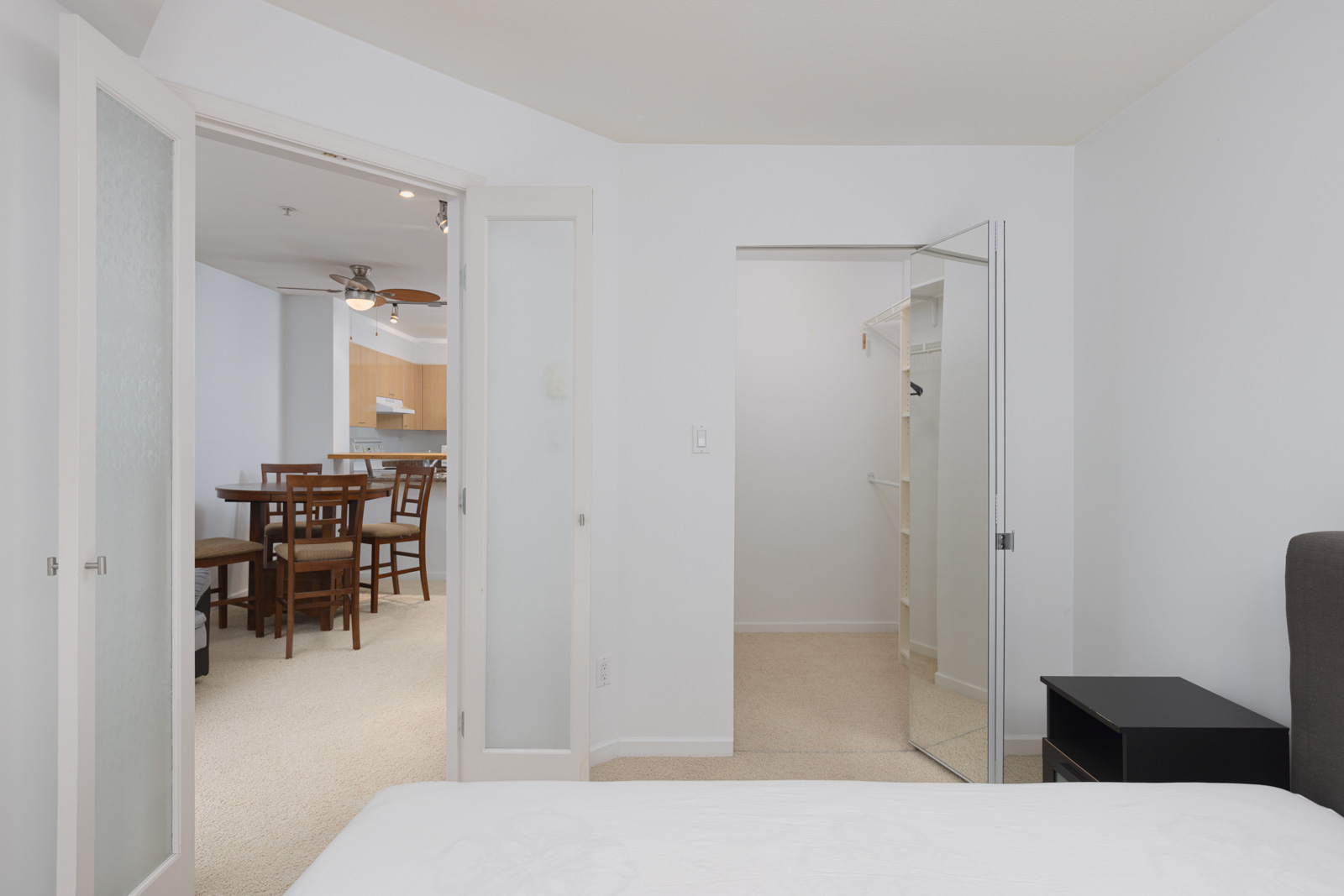 View from a bedroom showing double doors opening to a dining area and an open walk-in closet with mirrored sliding doors on the right.