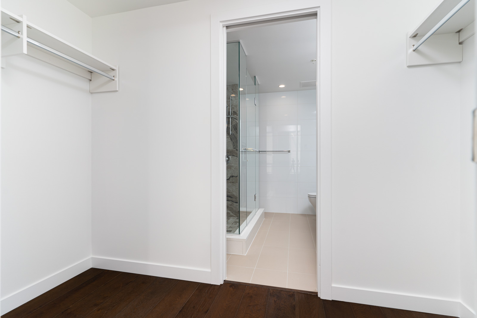 A walk-in closet with empty shelves and a sliding door leading to a bathroom with a glass-enclosed shower.