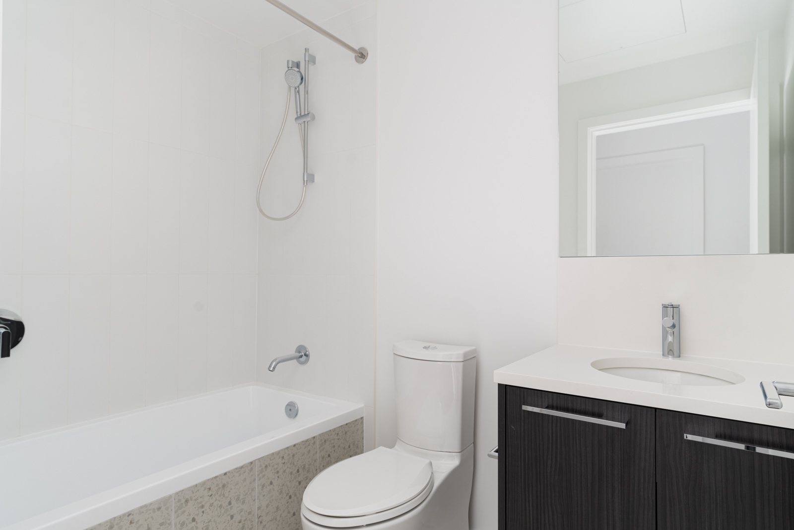 A modern bathroom with a bathtub and shower, a white toilet, and a vanity with a sink and large mirror.