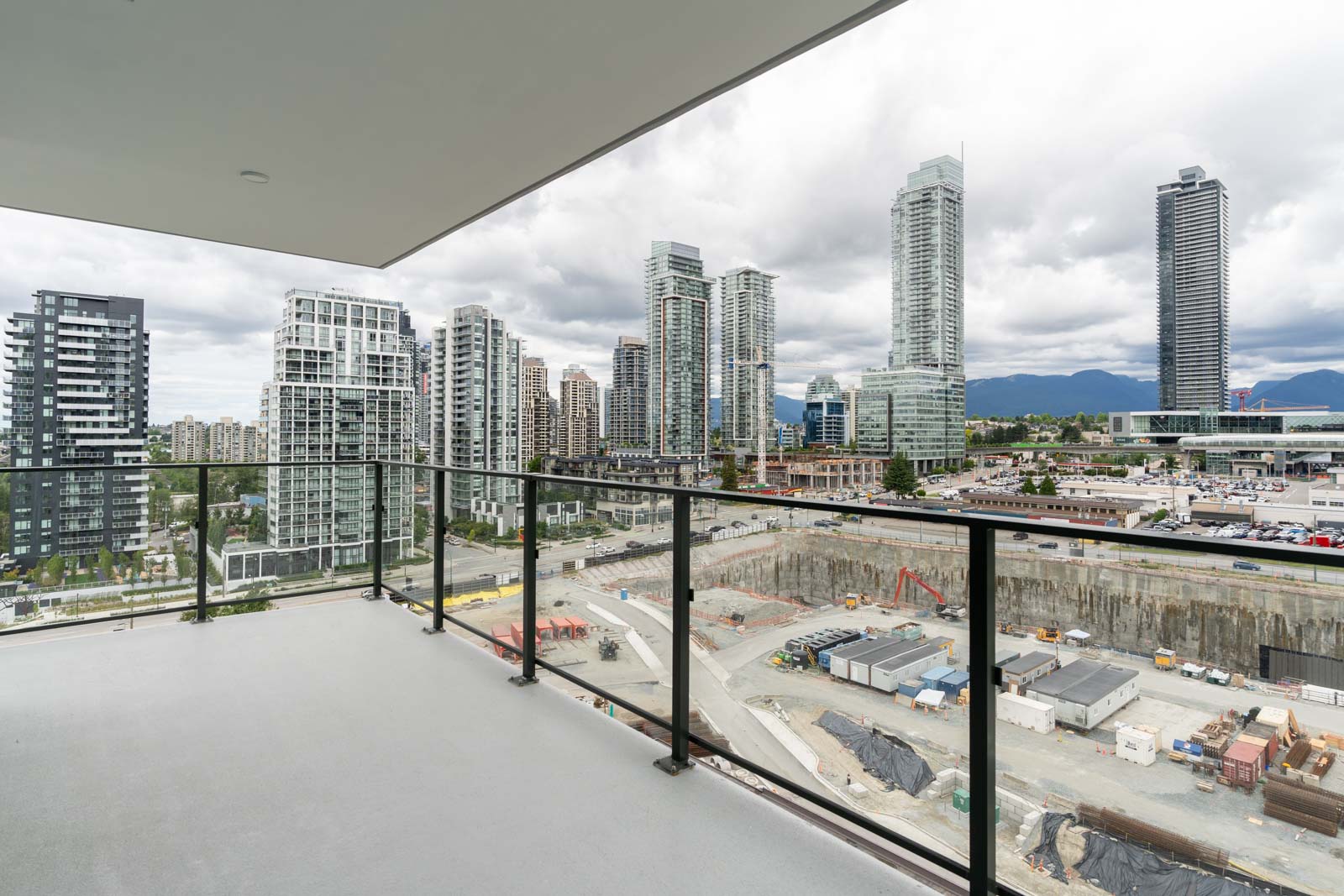 View from a high-rise balcony overlooking a cityscape with modern buildings, construction site below, and cloudy sky in the background.