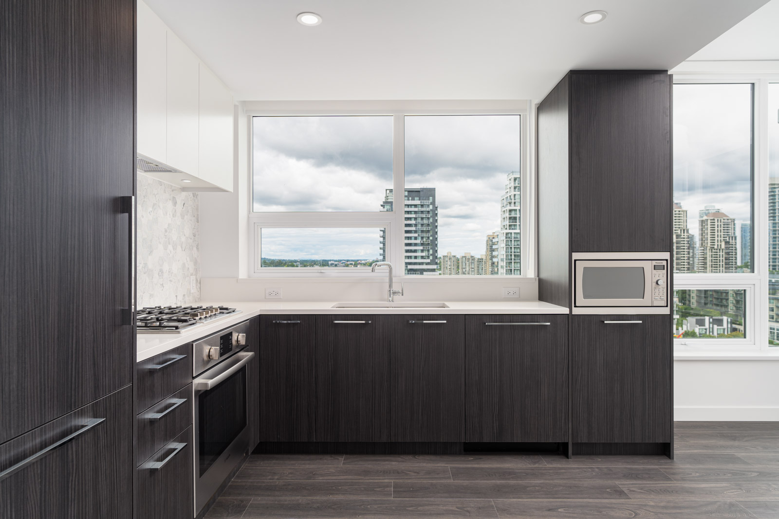 Modern kitchen with dark wood cabinets, stainless steel appliances, a large window with city views, and white countertops.