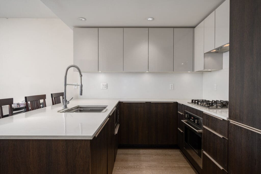 Modern kitchen with dark wood lower cabinets, glossy white upper cabinets, built-in oven, gas stove, stainless steel sink, and a pull-down faucet.