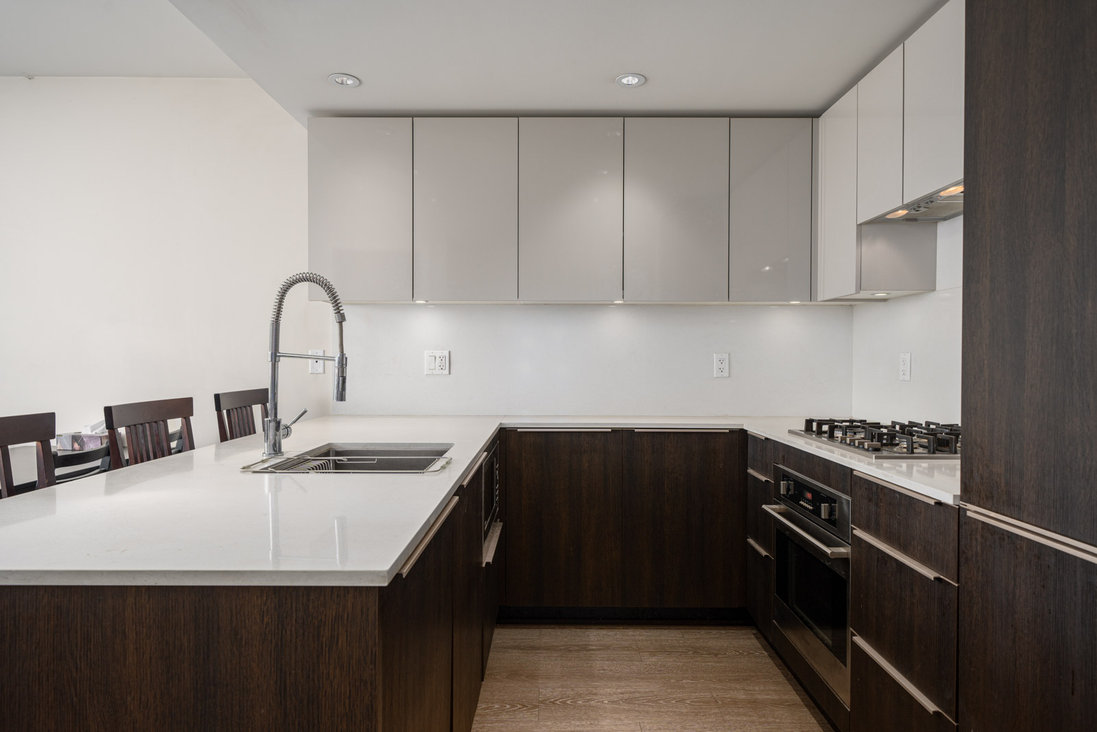 Modern kitchen with dark wood lower cabinets, glossy white upper cabinets, built-in oven, gas stove, stainless steel sink, and a pull-down faucet.