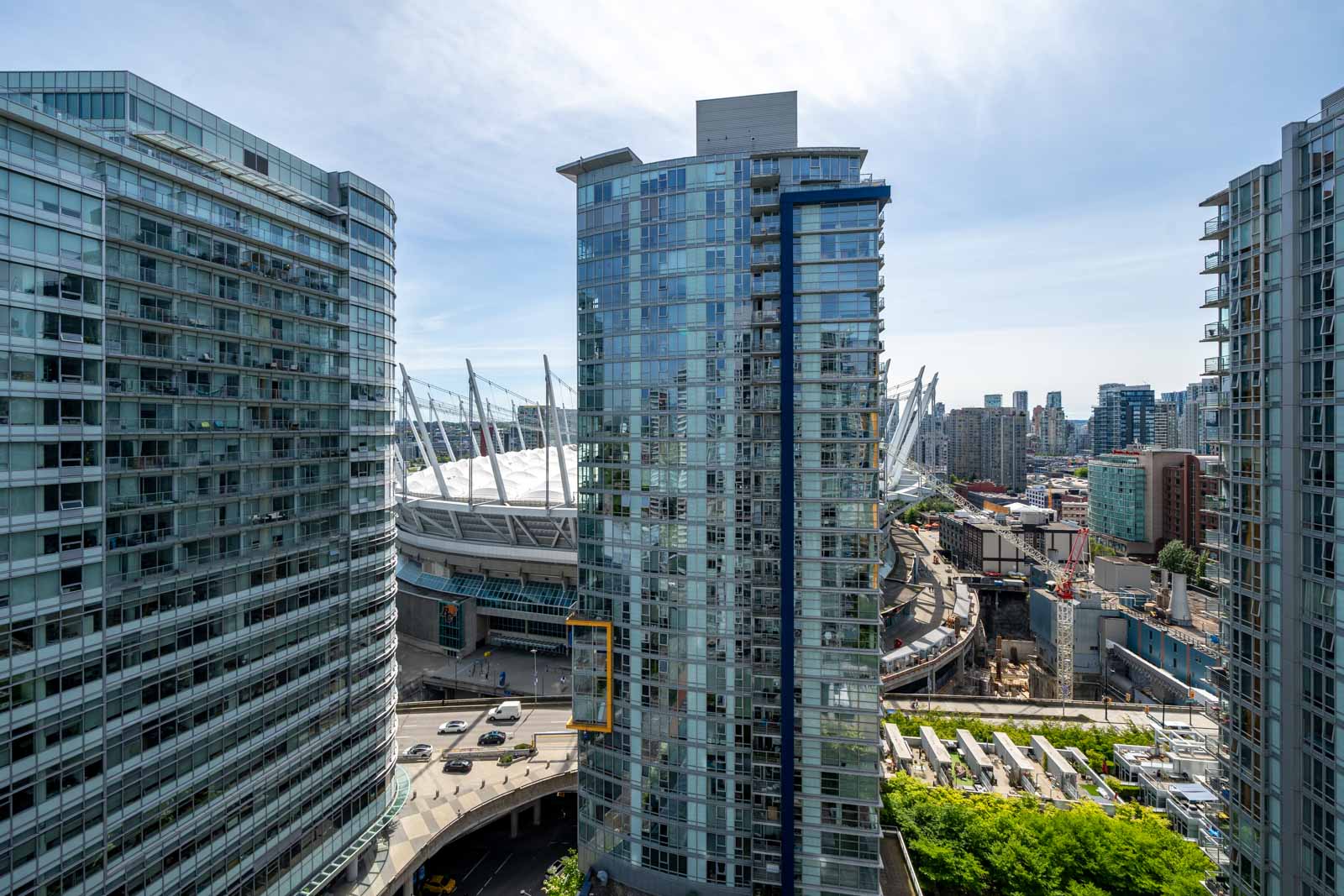 High-rise glass apartment buildings with a sports stadium in the background, busy roads, and city structures under a clear sky.
