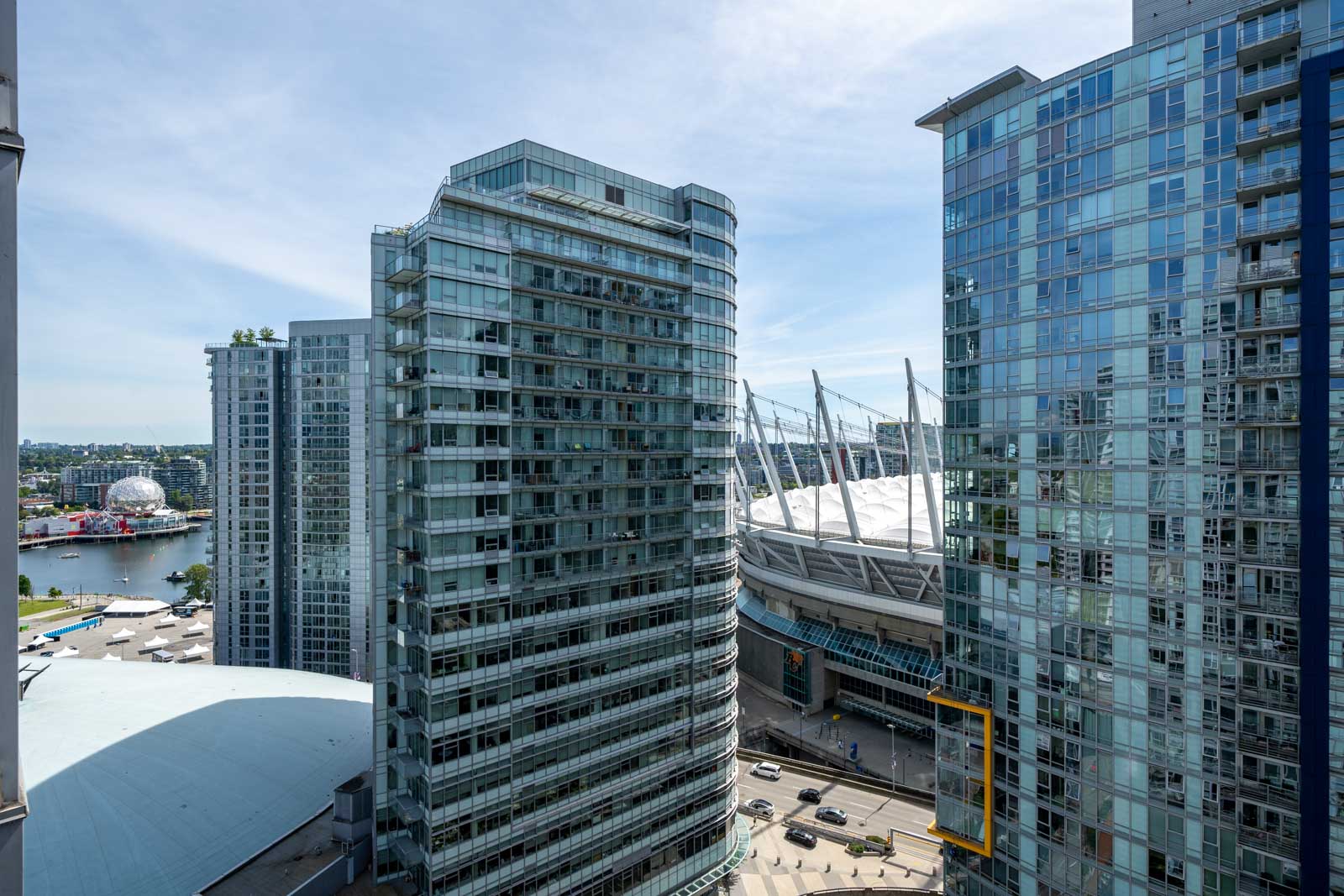 High-rise glass buildings with a view of BC Place Stadium and surrounding cityscape on a clear day.