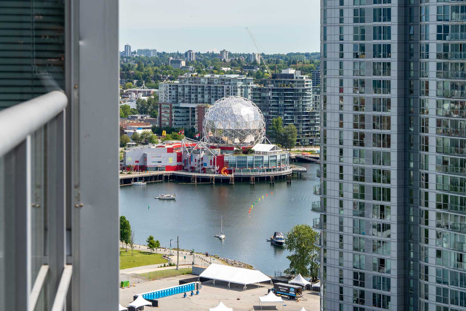 View of a waterfront science museum with a geodesic dome, surrounded by modern high-rise buildings and boats on the water.