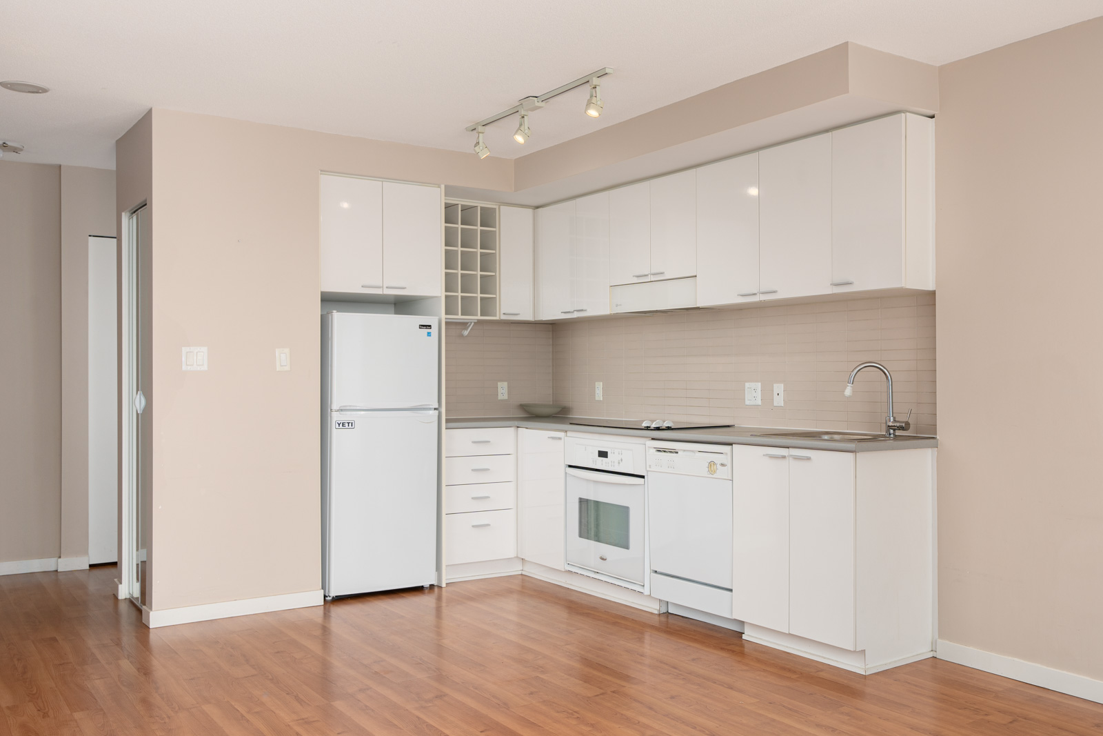 Modern kitchen with white cabinets, appliances including a fridge, oven, and dishwasher, under-cabinet lighting, and light wood flooring.