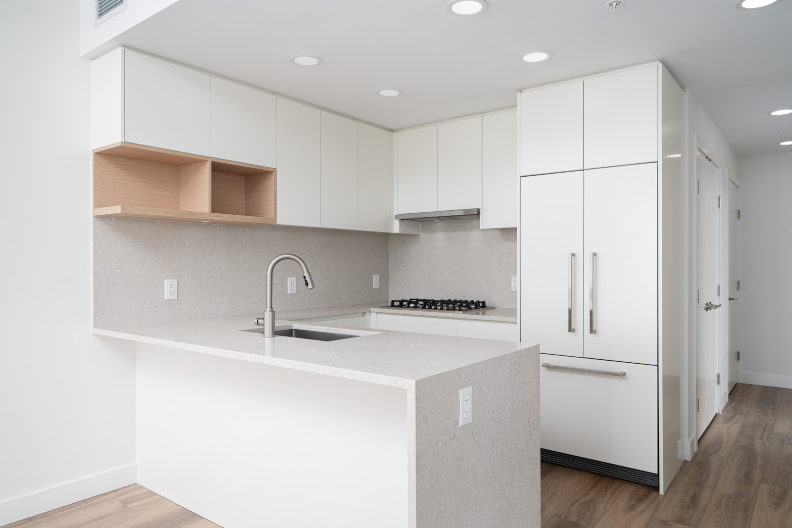 Modern kitchen with white cabinets, built-in appliances, gas stove, under-mount sink, and light wood flooring.