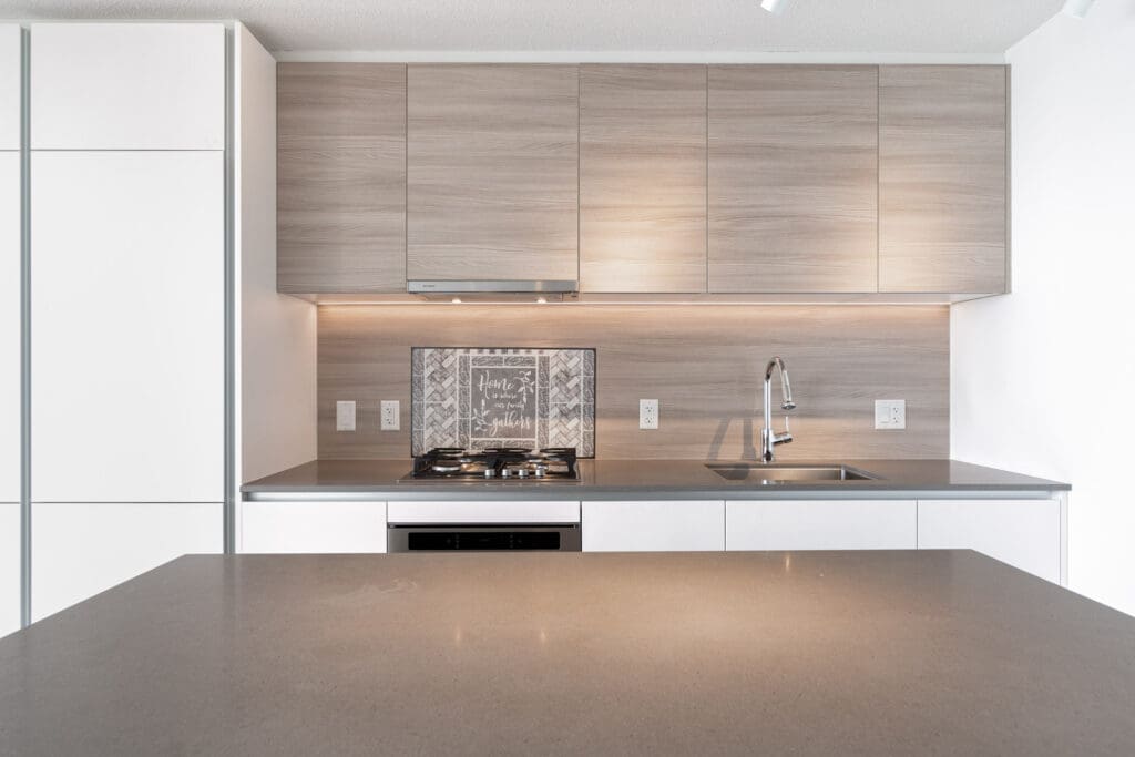 Modern kitchen with light wood cabinets, built-in stove, oven, and sink, featuring neutral countertops and a minimalist backsplash.
