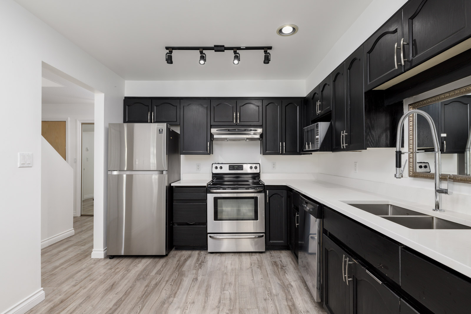 Modern kitchen with black cabinets, stainless steel appliances, white countertops, and light wood flooring.