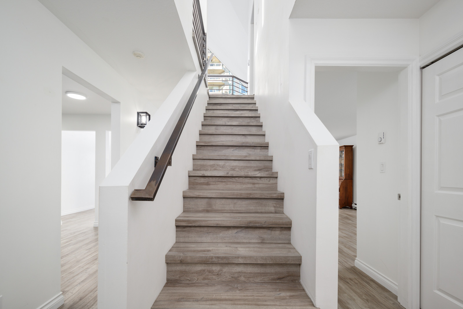 A straight staircase with wooden steps and a simple handrail leads up between white walls in a modern home interior.
