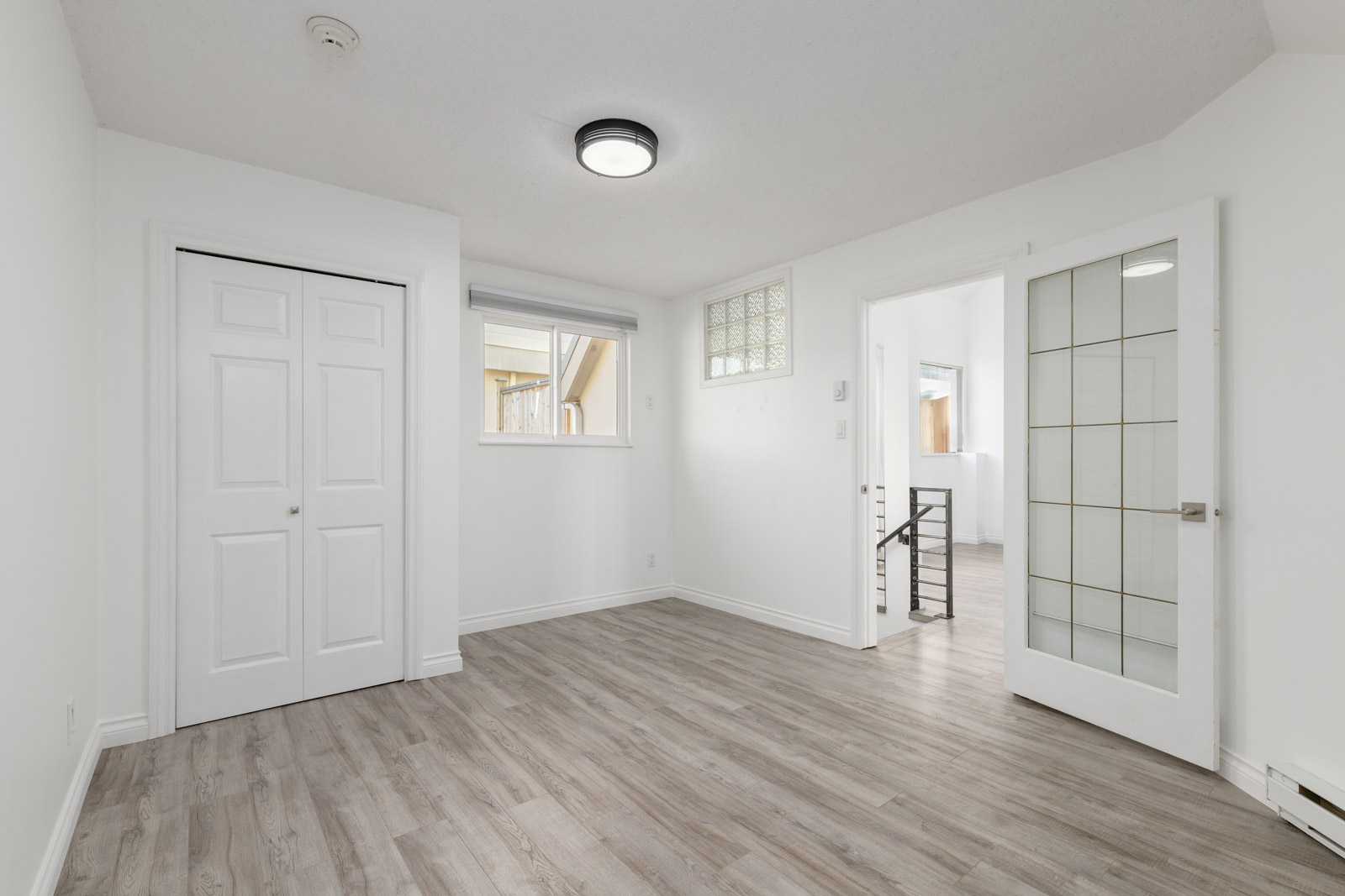 Empty white room with wood flooring, a closed closet, a window, a glass-paneled door, and a ceiling light.