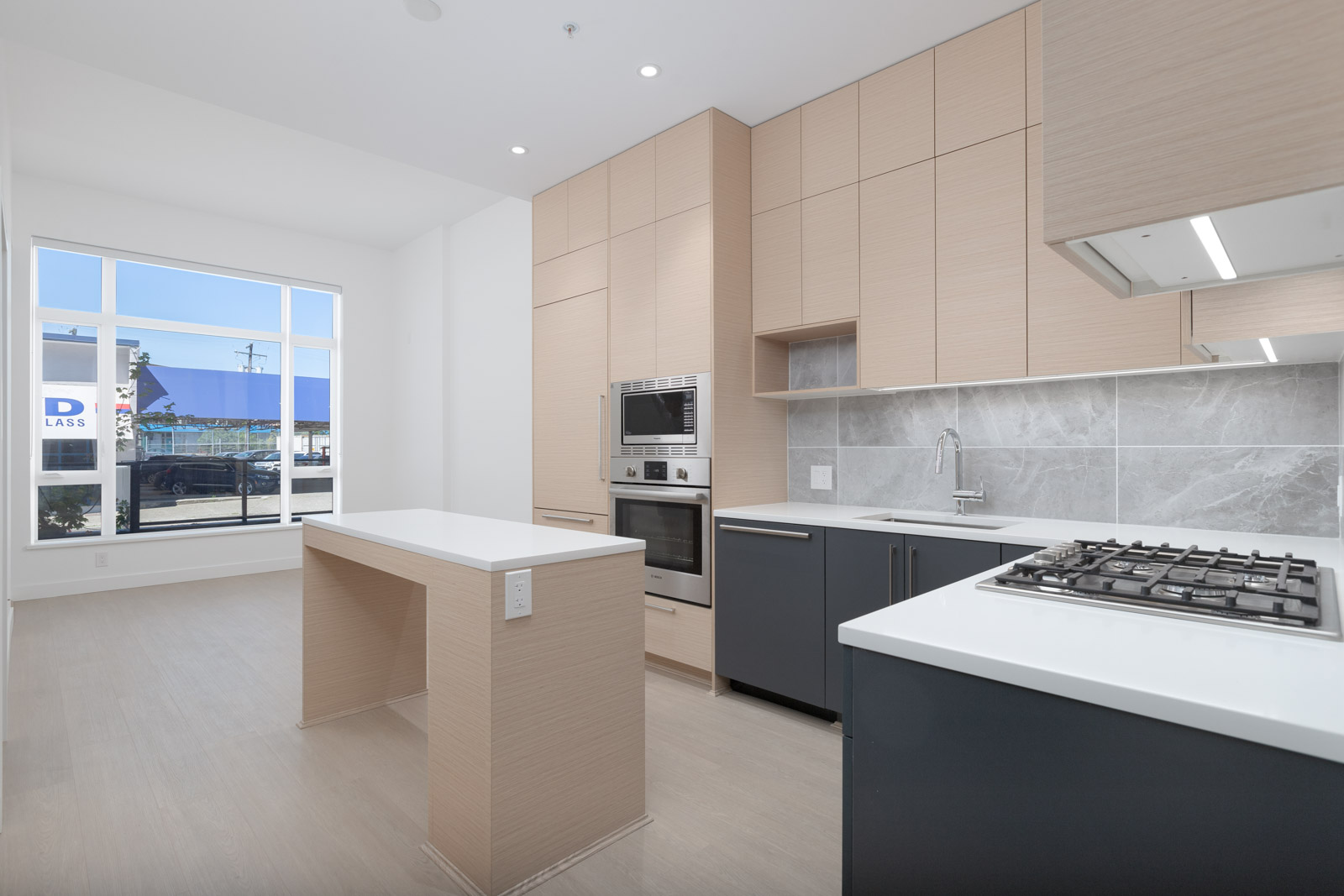 Modern kitchen with light wood cabinets, a center island, built-in oven and microwave, gas stove, and large window letting in natural light.