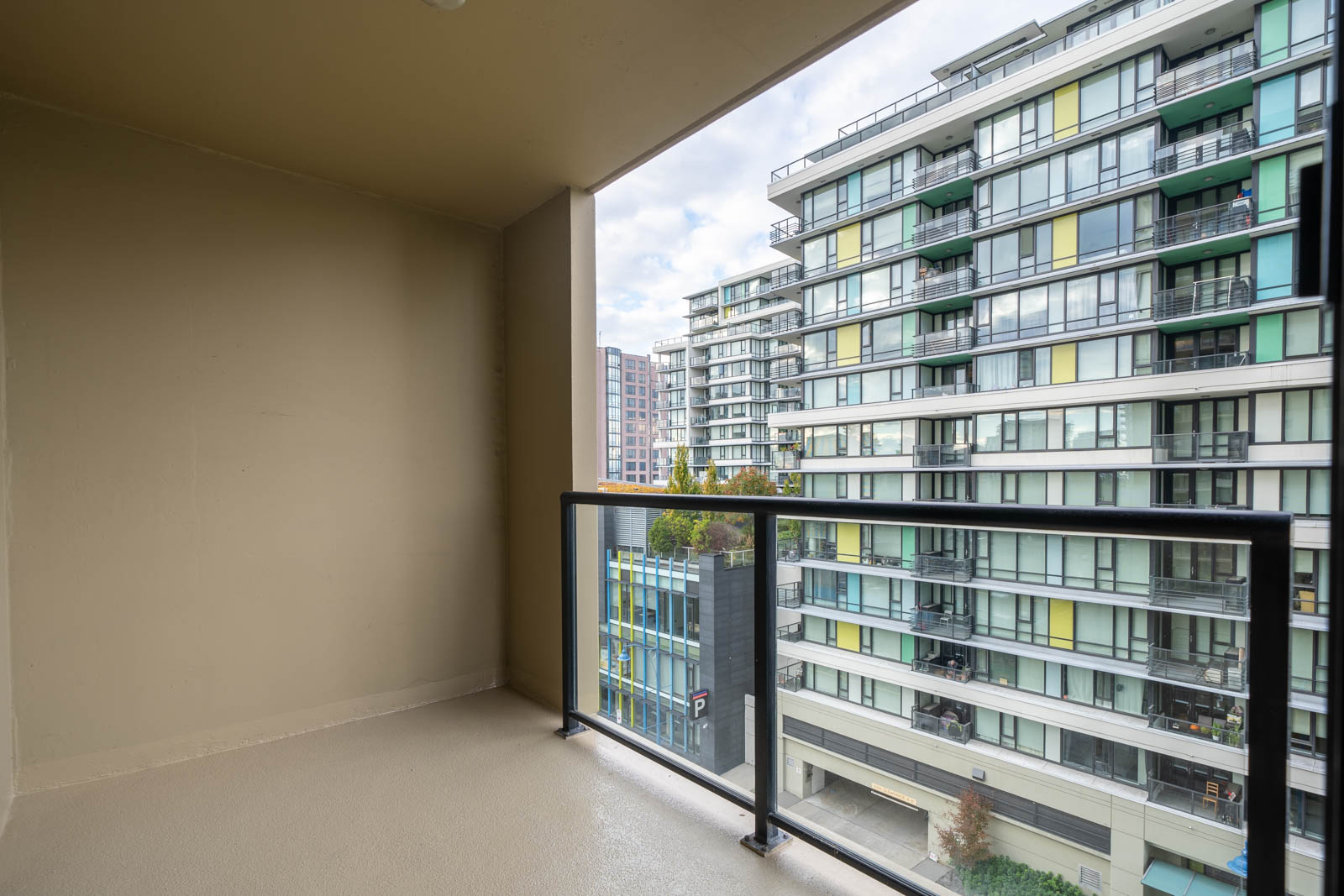 A view from an empty apartment balcony with a glass railing, overlooking modern multi-story residential buildings.