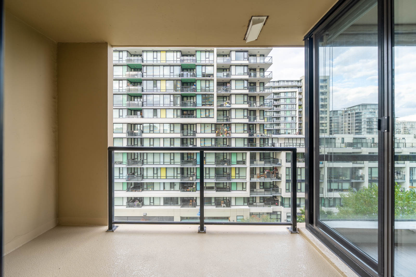 View from an empty balcony with beige flooring, looking out toward a modern apartment building with glass balconies and large windows.