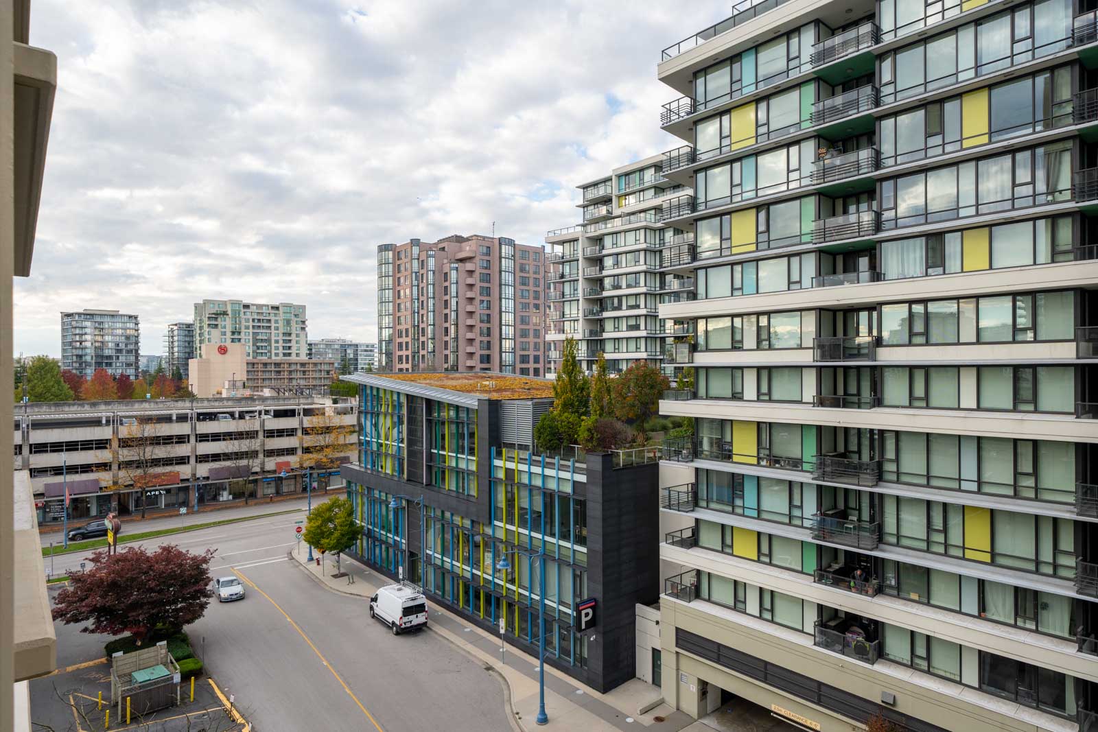 A view of modern mid-rise apartment buildings and a street with a parked white van, seen from a higher floor on a cloudy day.