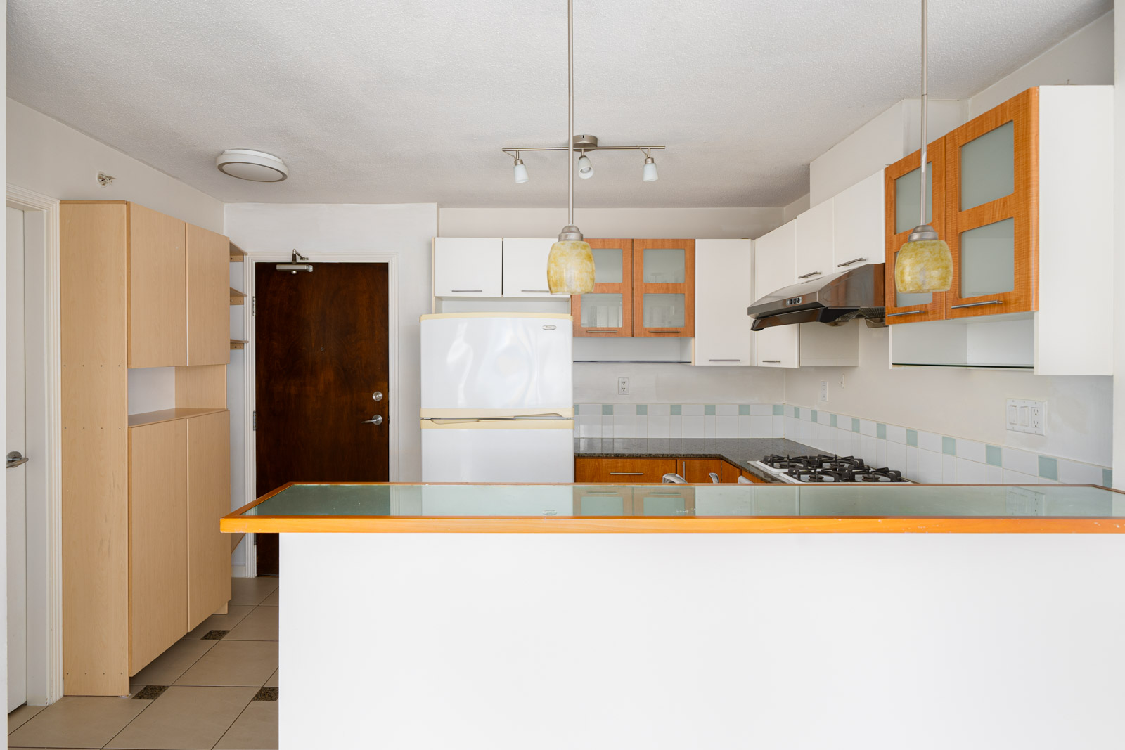 Modern kitchen with white cabinets, wooden accents, a glass countertop, gas stove, refrigerator, and pendant lighting.