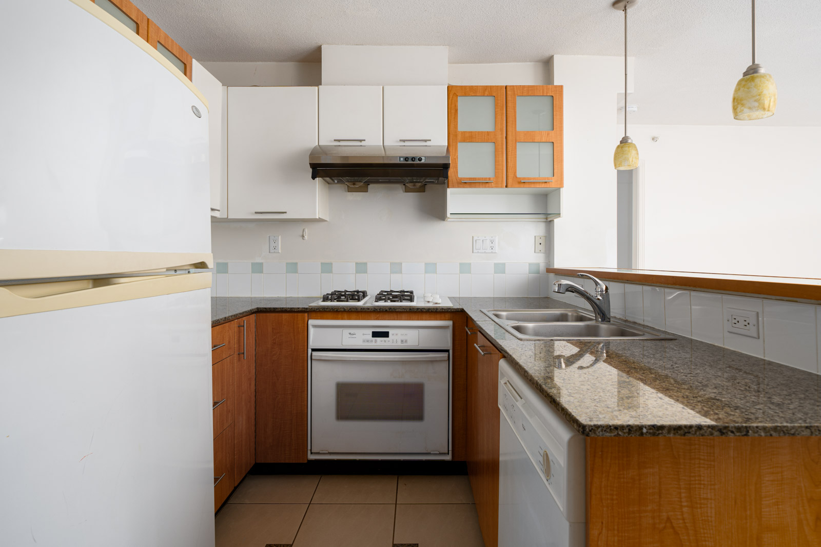 Modern kitchen with wooden and white cabinets, granite countertops, built-in oven, gas cooktop, double sink, dishwasher, and a refrigerator.