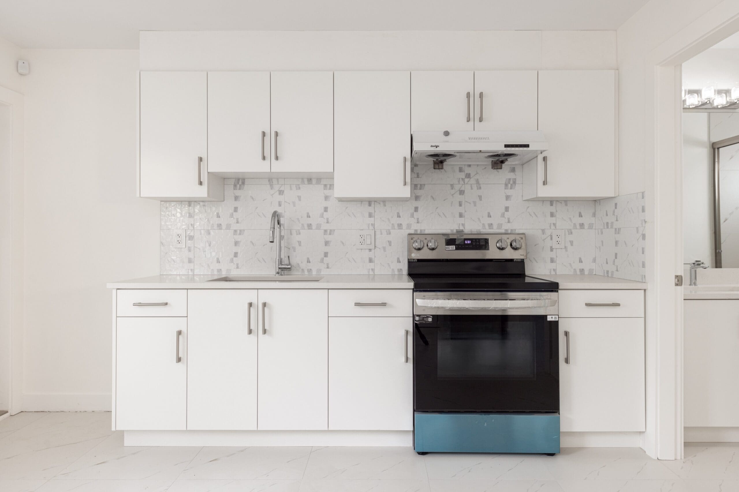 Modern kitchen with white cabinets, tiled backsplash, built-in sink, and a stainless steel oven with a stove, set against a clean, minimalist backdrop.
