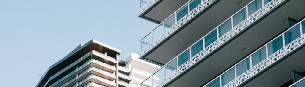 Close-up view of two modern high-rise apartment buildings with balconies against a clear blue sky.