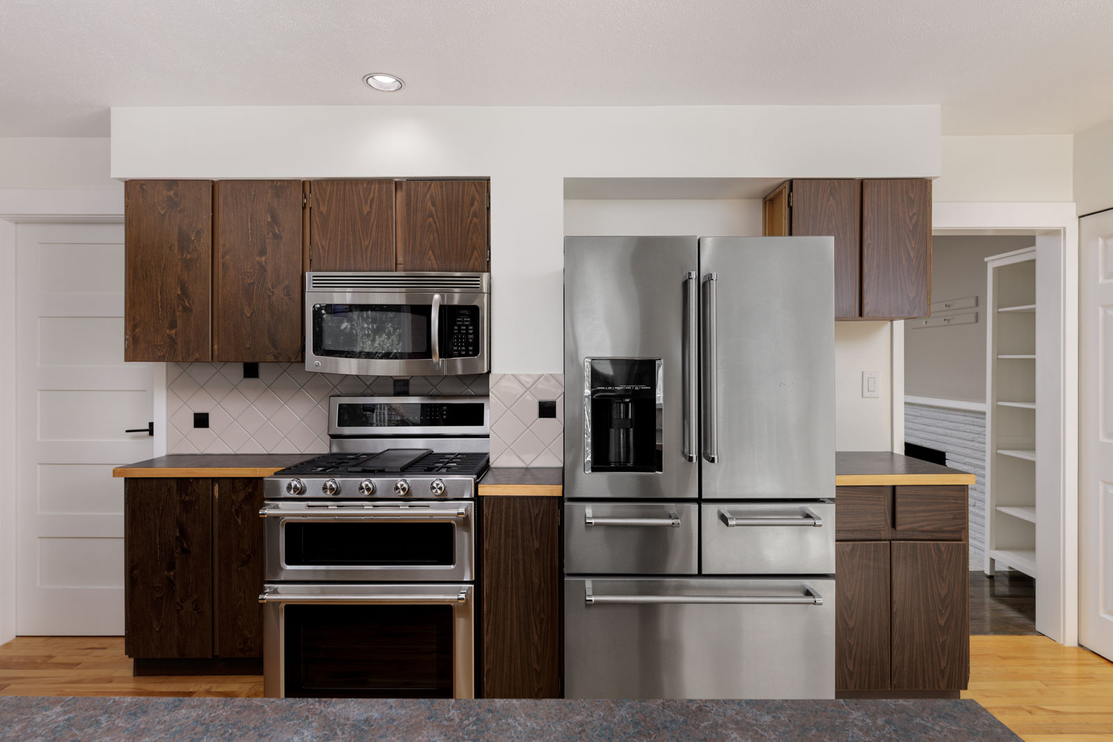 Modern kitchen with dark wood cabinets, stainless steel appliances including a stove, microwave, and French door refrigerator, and a white tile backsplash.
