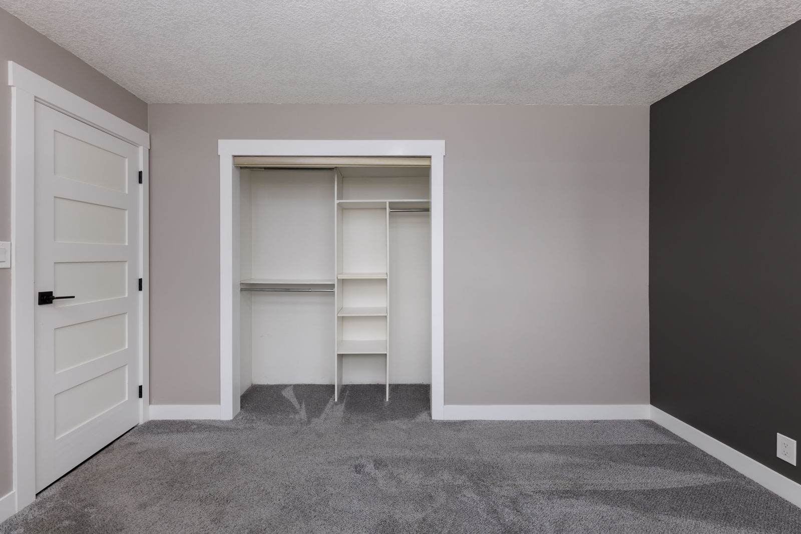 Empty room with gray carpet, light gray walls, a white door, and an open closet with built-in shelves and hanging rods.