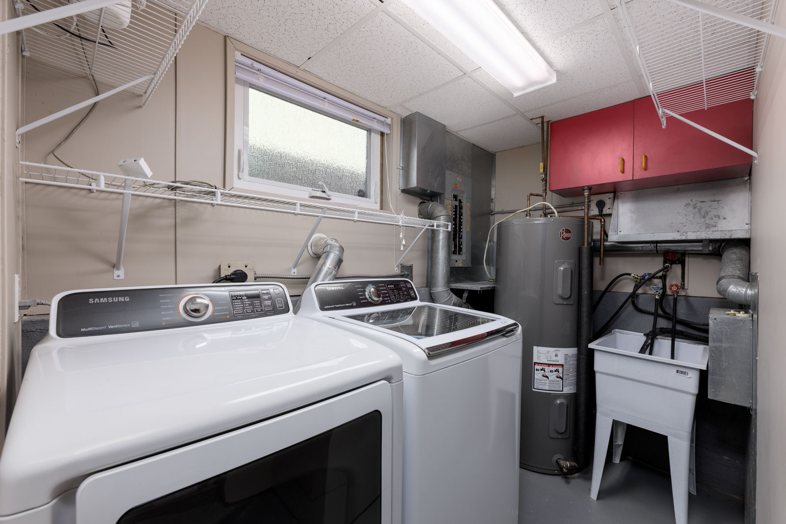 Laundry room with a washing machine and dryer, water heater, utility sink, wall shelves, and HVAC equipment under a small window.