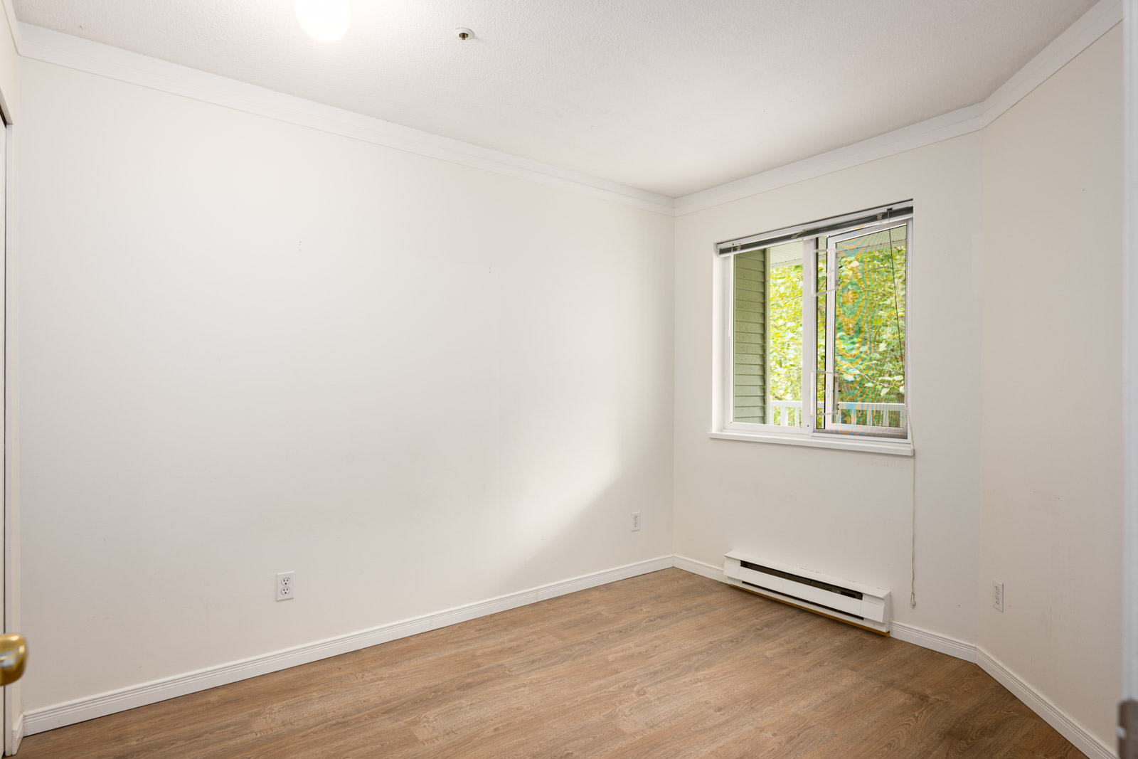 Empty room with white walls, a window with blinds, ceiling light, baseboard heater, and wood-look flooring.