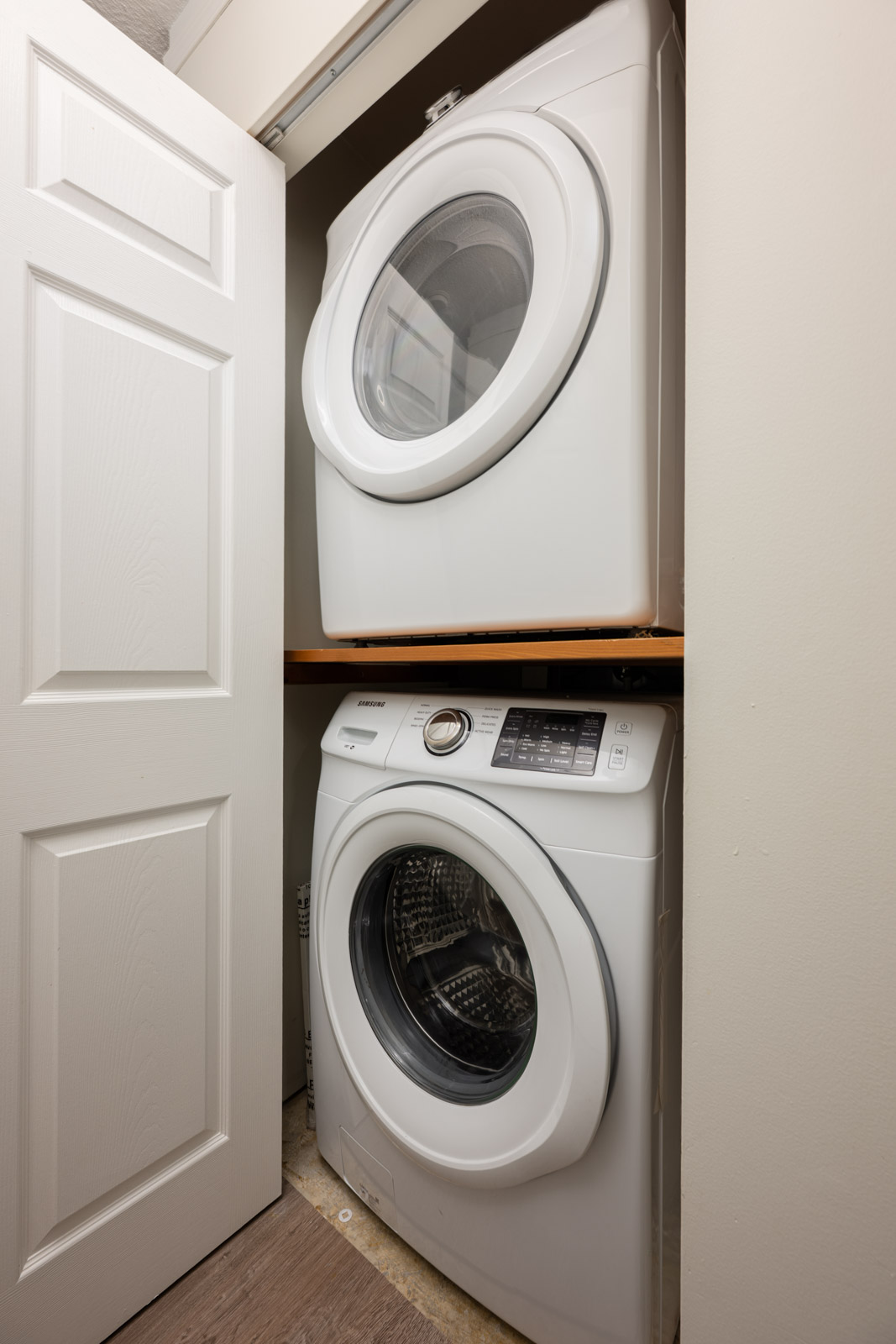 A stacked washer and dryer set inside a small closet with an open white door.