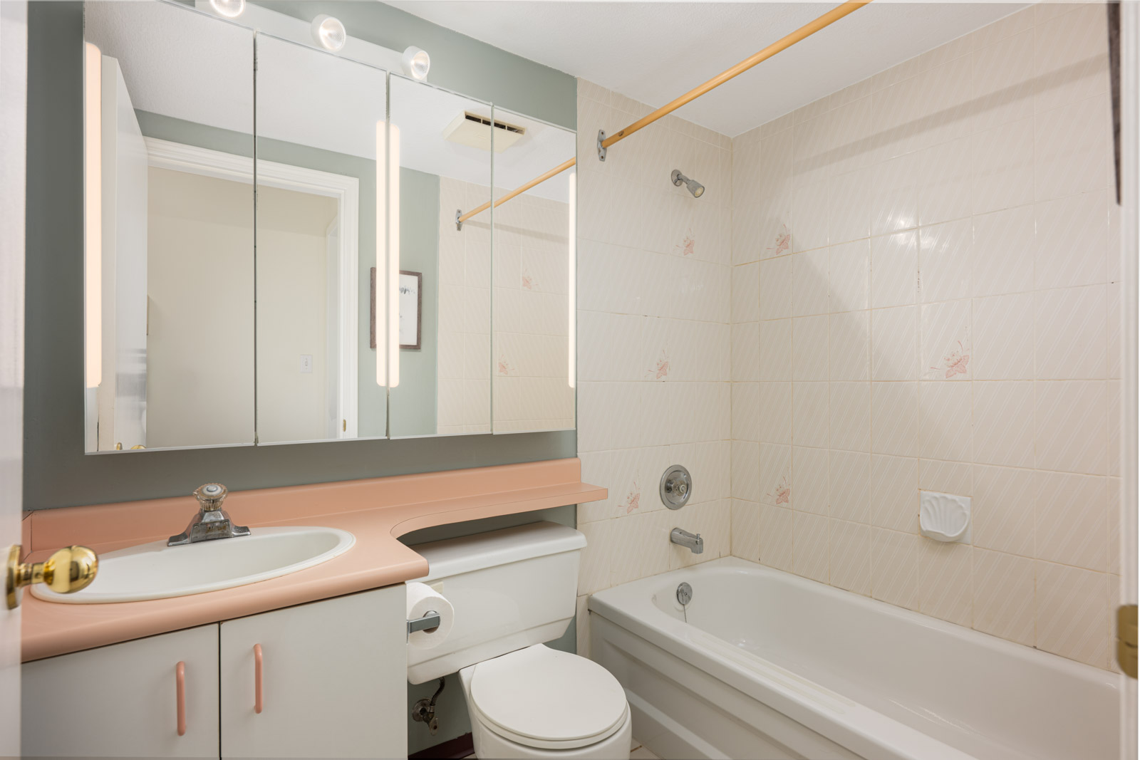 A small bathroom with a sink, mirrored cabinet, toilet, and bathtub with shower. The countertop is pink and tile walls have a light pattern.