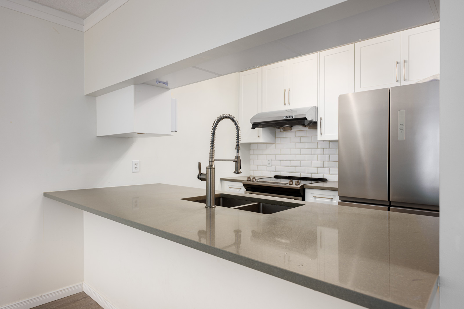Modern kitchen with gray countertop, stainless steel sink and faucet, white cabinets, subway tile backsplash, stove, and refrigerator.
