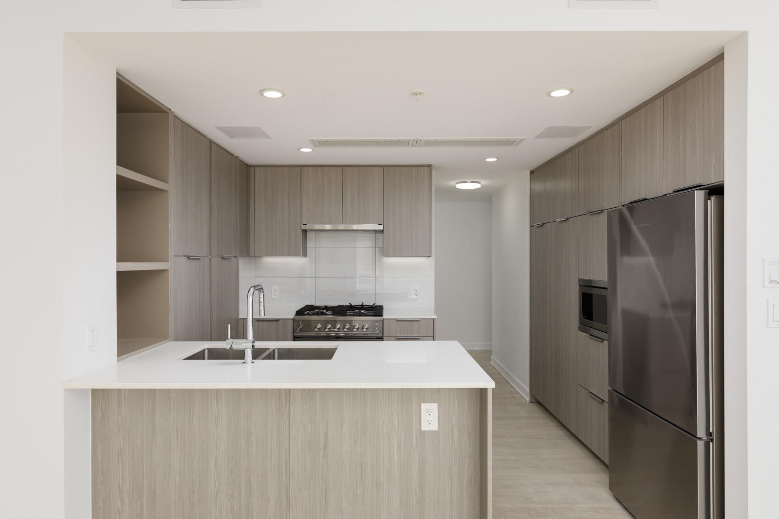 Modern kitchen with light wood cabinets, stainless steel appliances, white countertop island with sink, built-in oven, and gas stove under recessed lighting.