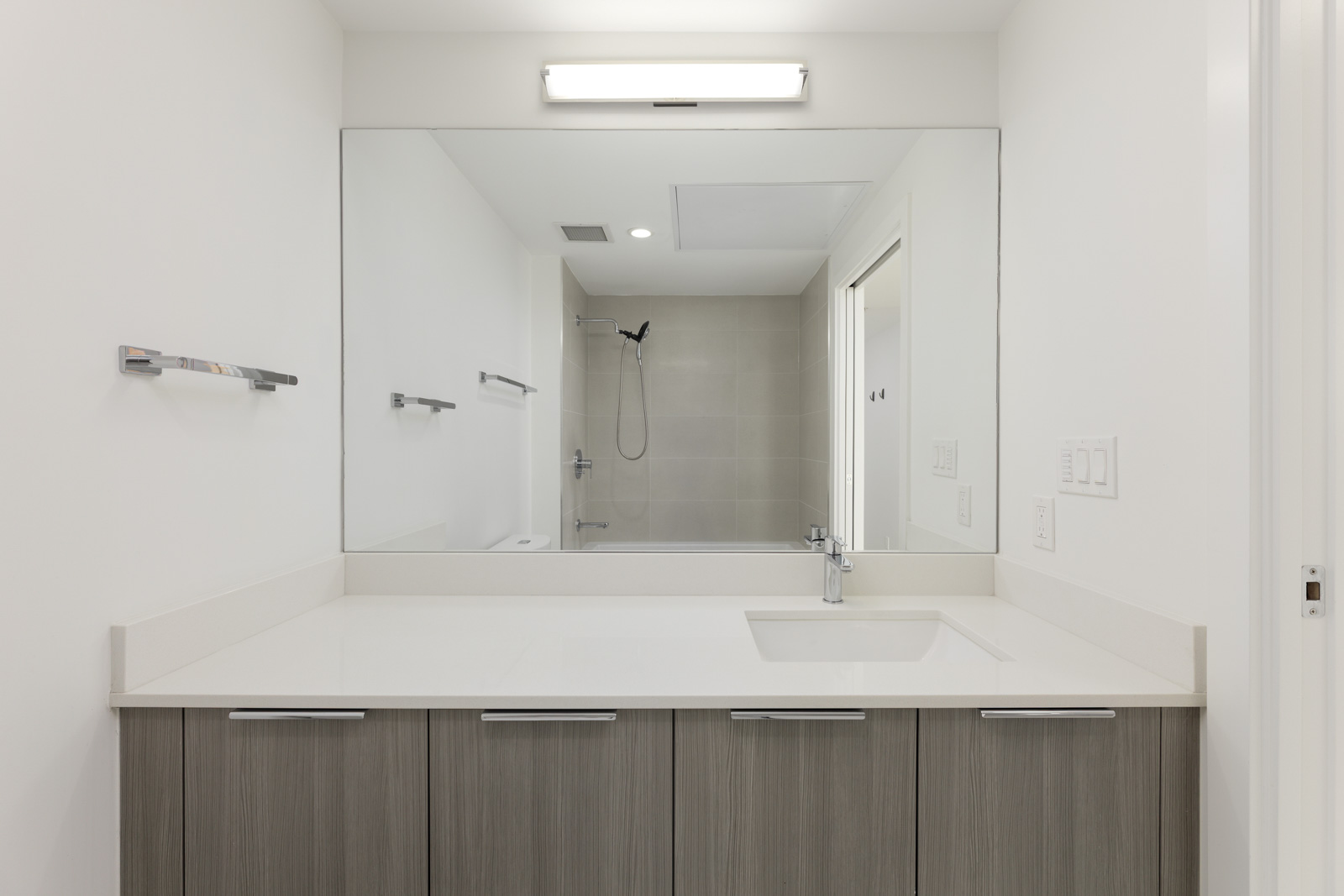 Modern bathroom with a large mirror, wall-mounted faucet, under-sink cabinets, towel racks, and a walk-in shower with a handheld showerhead.
