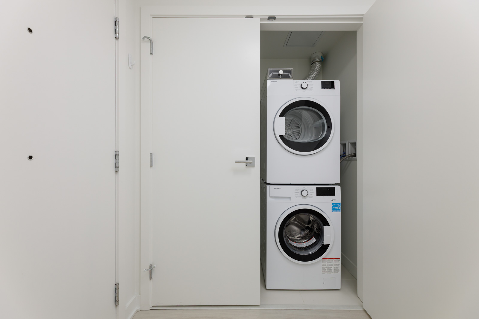 A stacked washer and dryer set is placed inside a small, white closet with the doors open.
