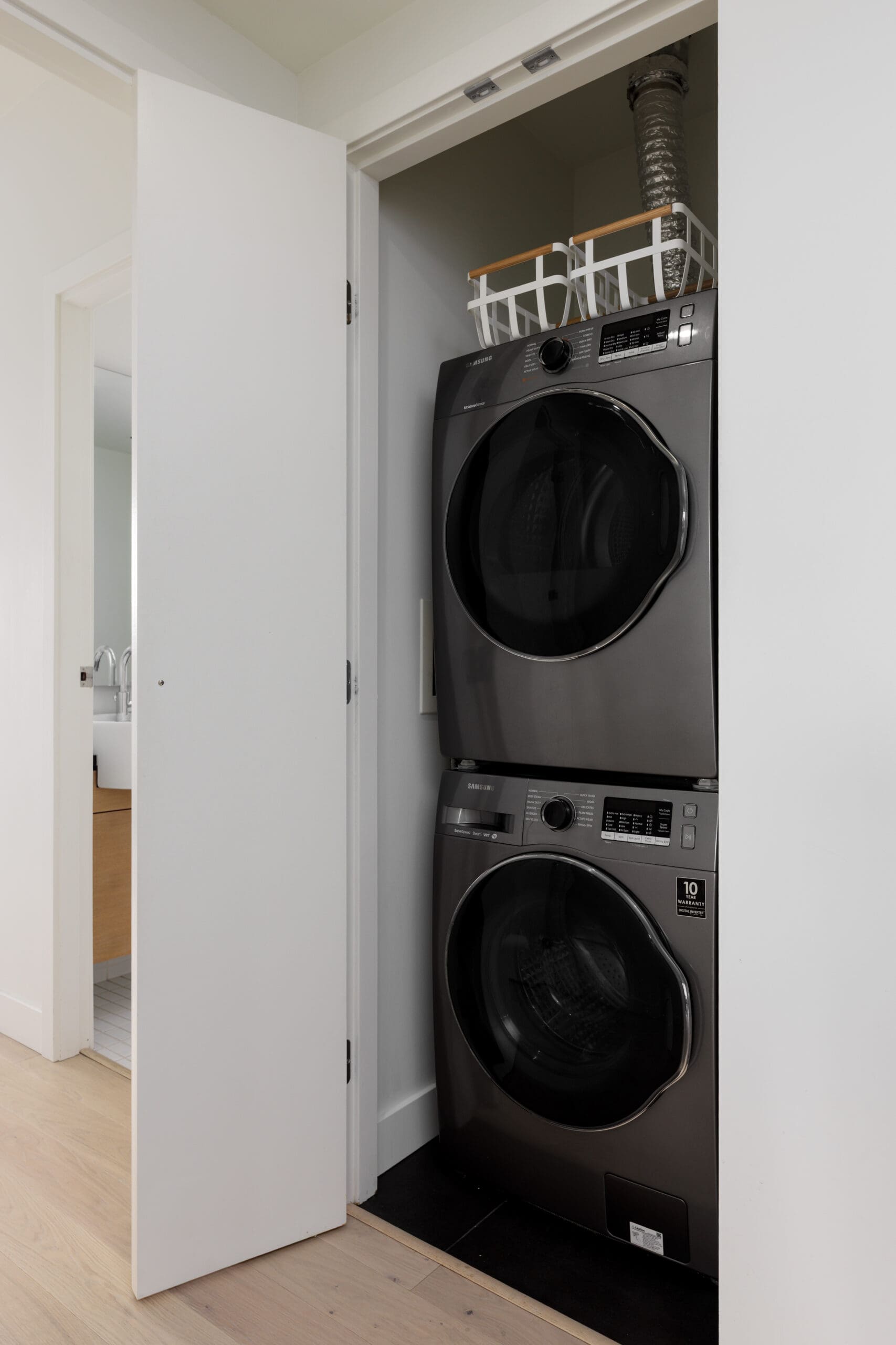 A stacked washer and dryer set in a small closet with a shelf holding laundry baskets above them.