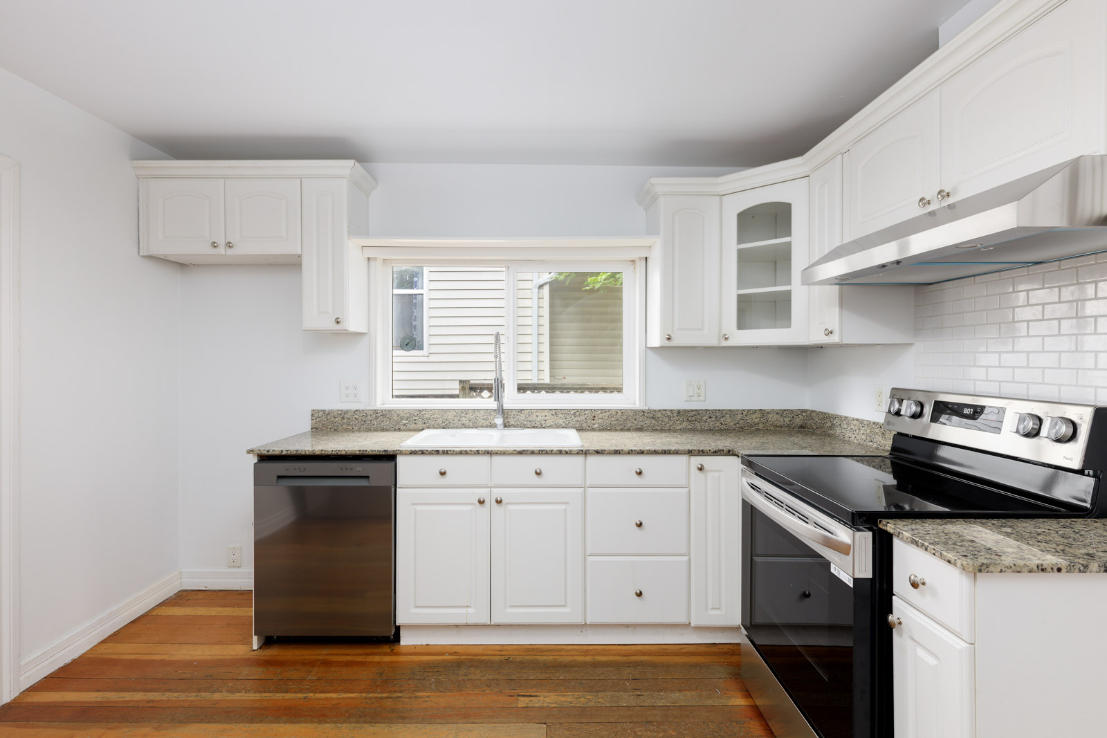 Modern kitchen with white cabinets, granite countertops, stainless steel appliances, and a window above the sink.