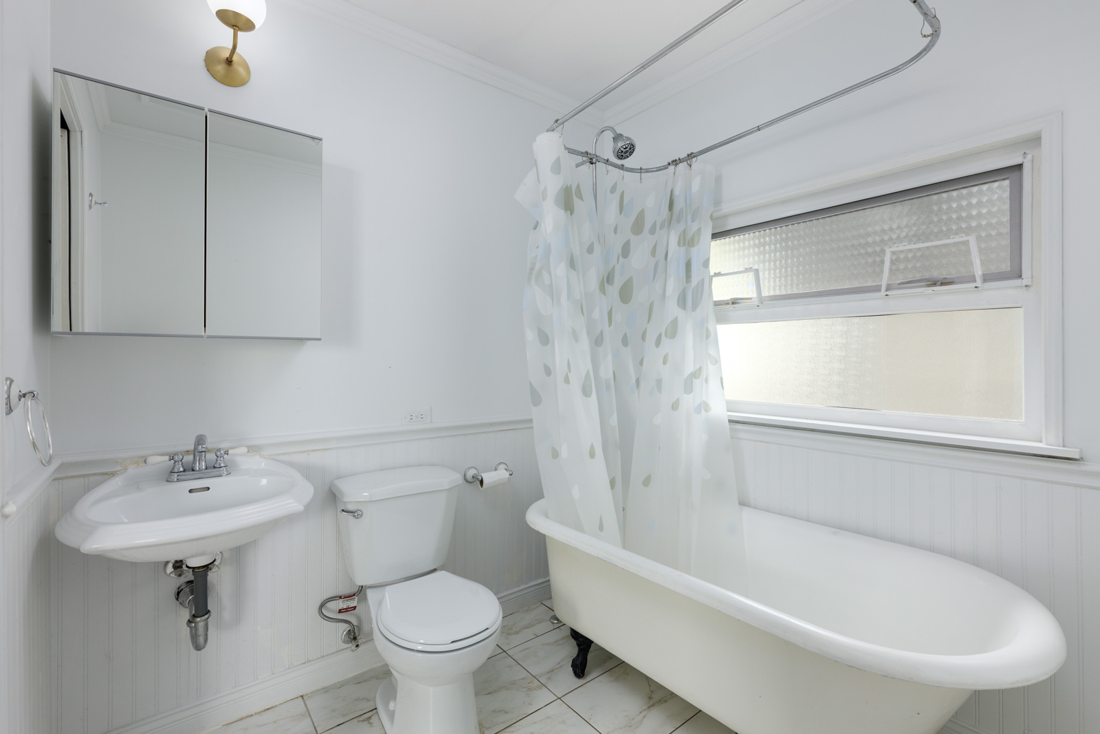 White bathroom with a pedestal sink, toilet, clawfoot tub with shower curtain, mirrored cabinet, wall light, and frosted window.
