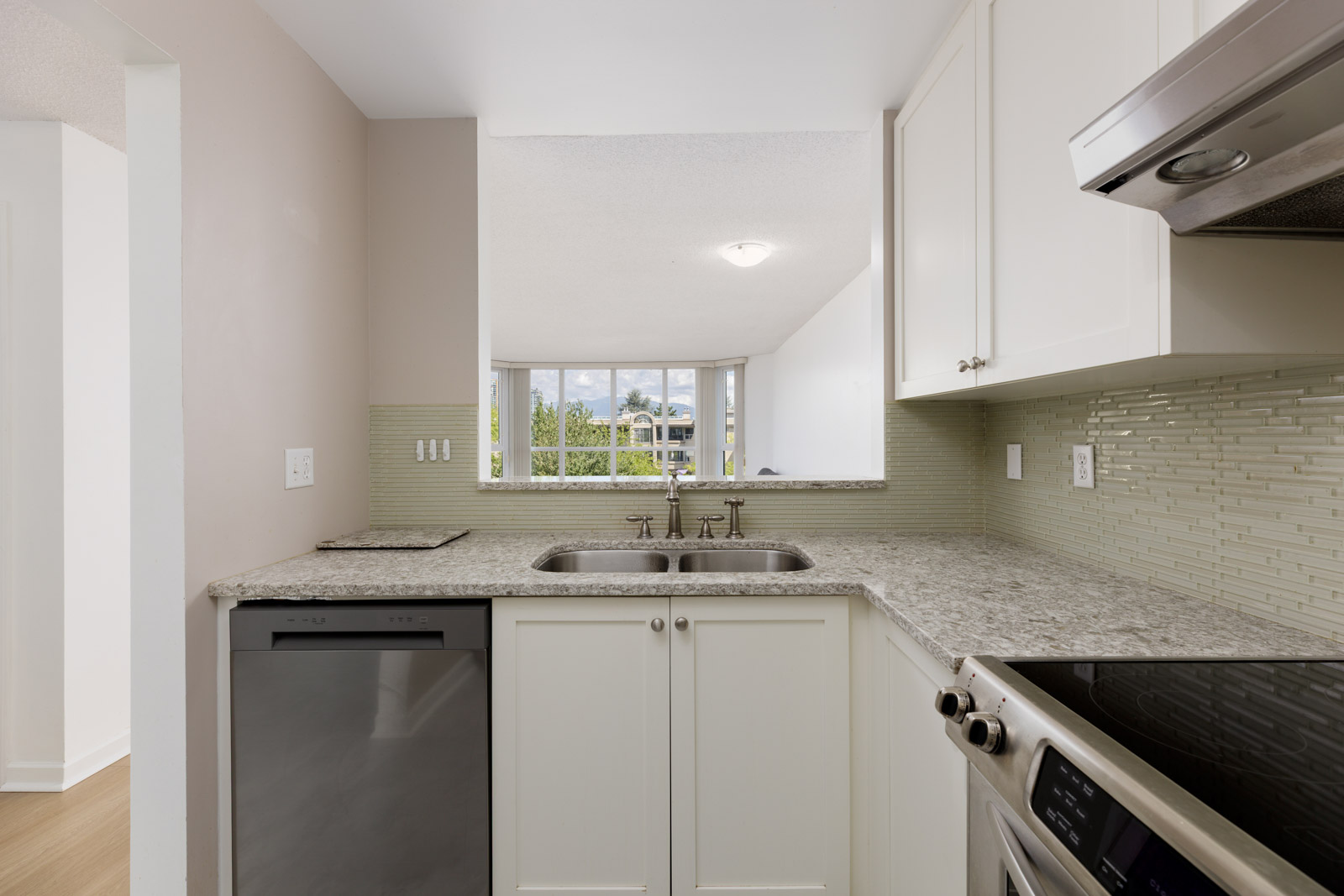 Modern kitchen with granite countertops, white cabinets, stainless steel appliances, tile backsplash, and a double sink facing a window with outdoor view.