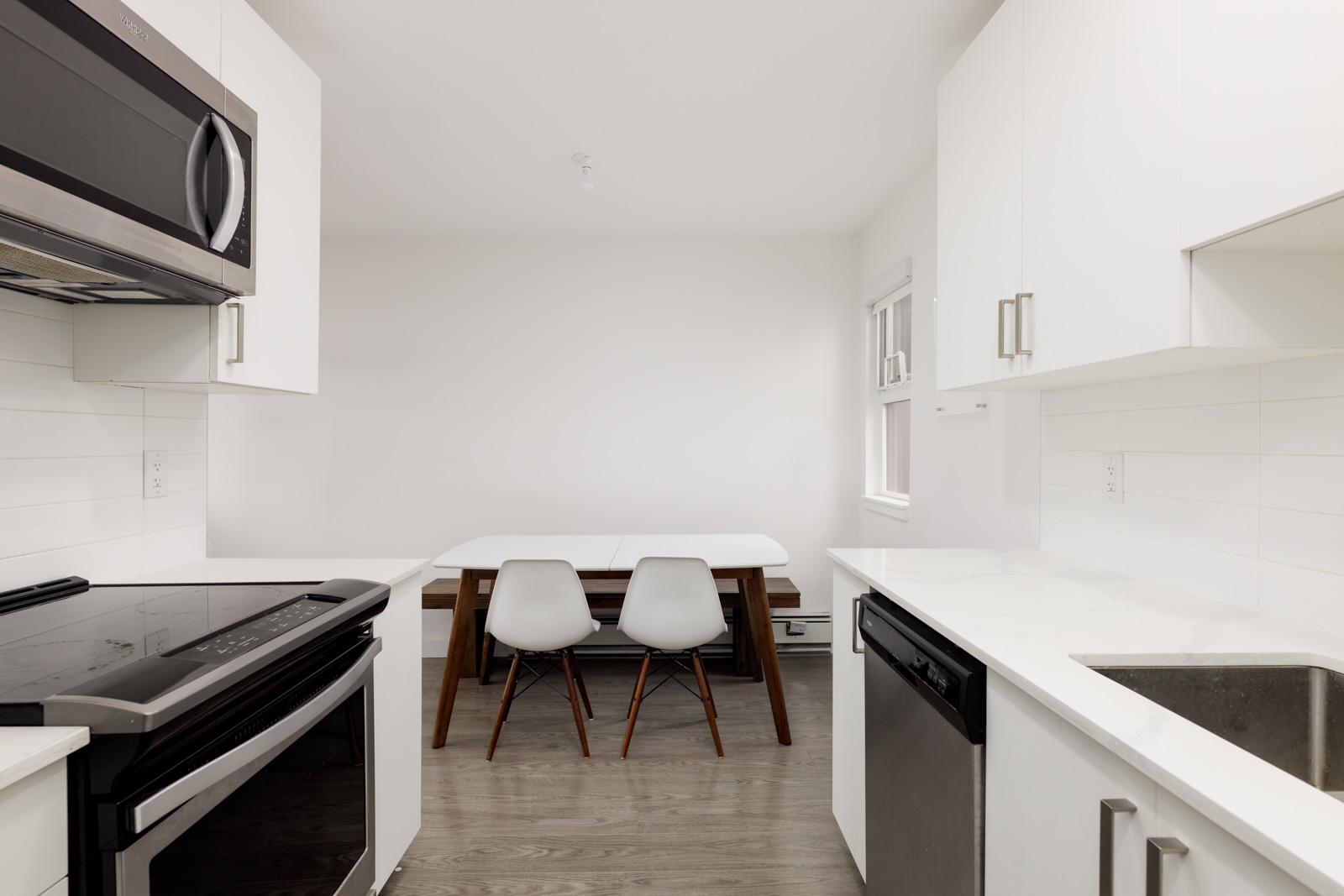 Modern kitchen with white cabinets, stainless steel appliances, a small dining table, and two white chairs in a clean, minimalist setting.
