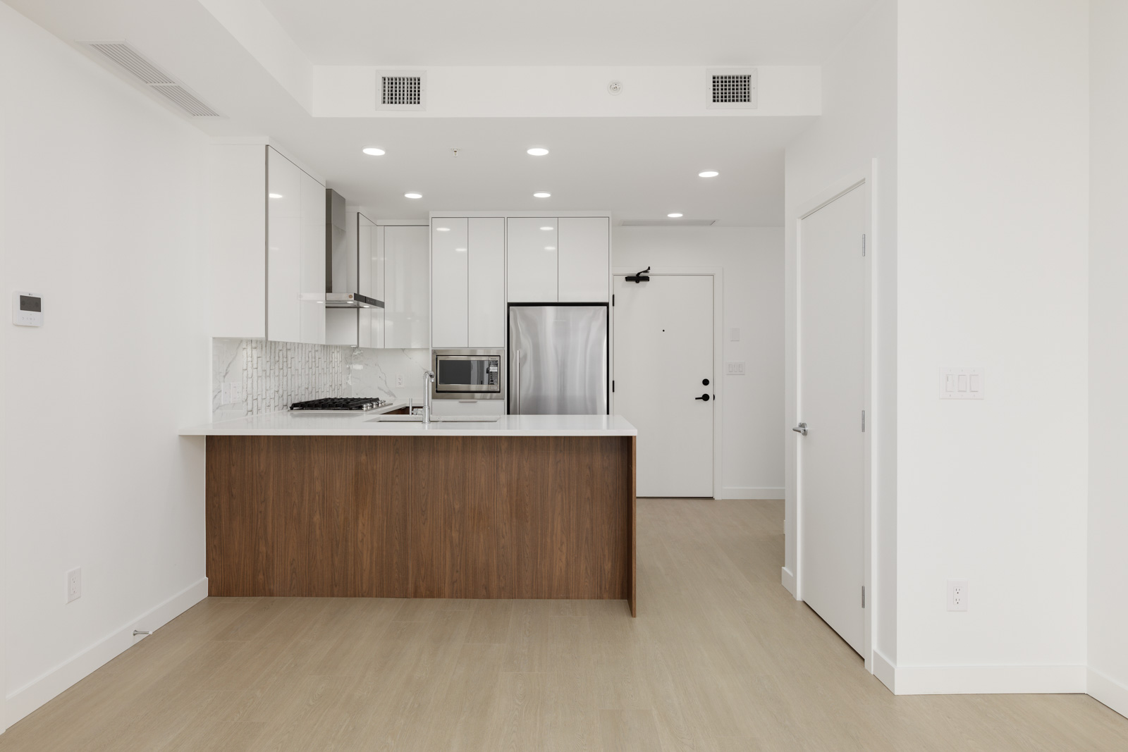 Modern kitchen with white cabinets, stainless steel appliances, a wood-paneled island, and light wood flooring in a bright, minimalist apartment.