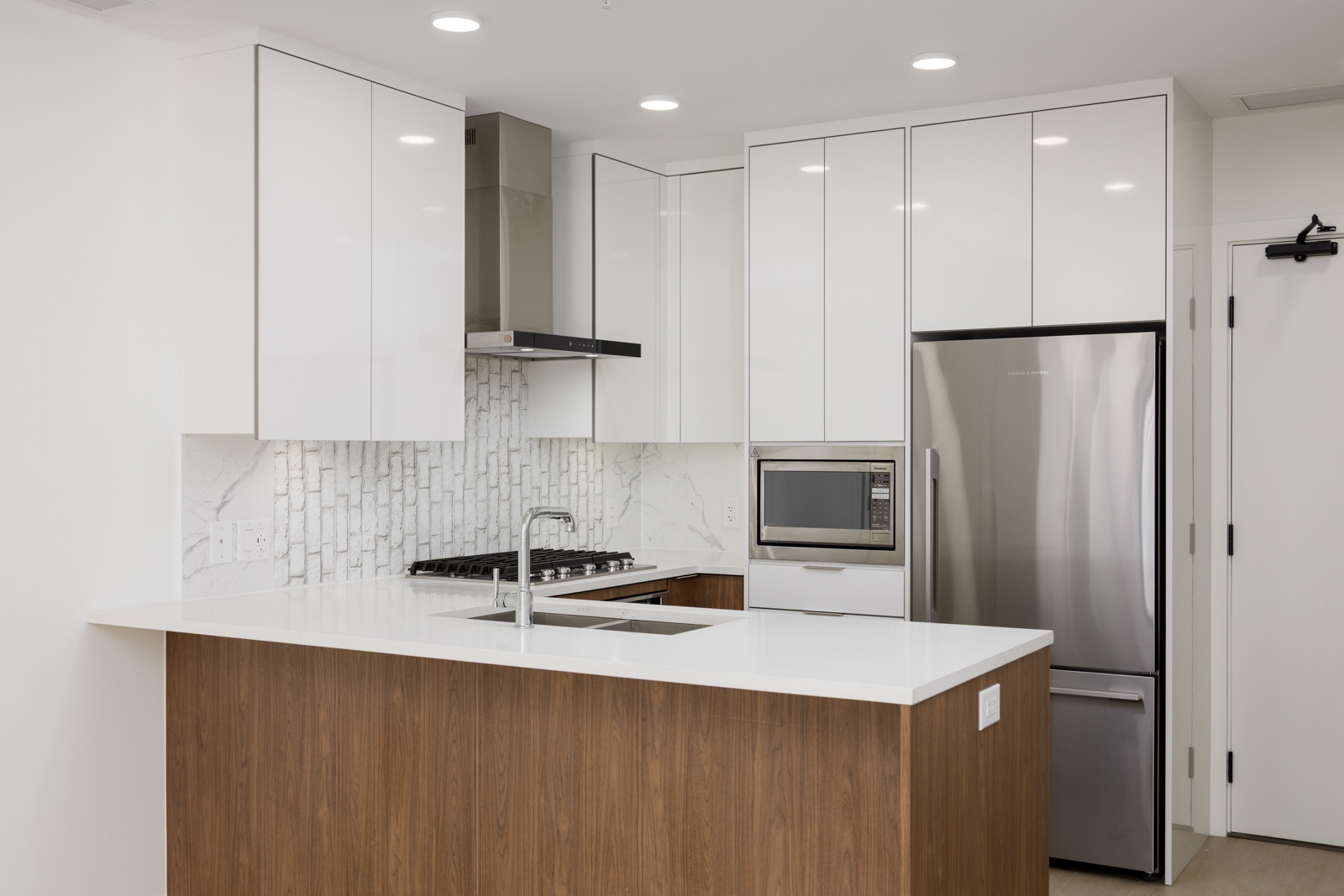 Modern kitchen with white cabinets, stainless steel appliances, a built-in microwave, a gas stove, and a wood-paneled island with a sink under bright ceiling lights.