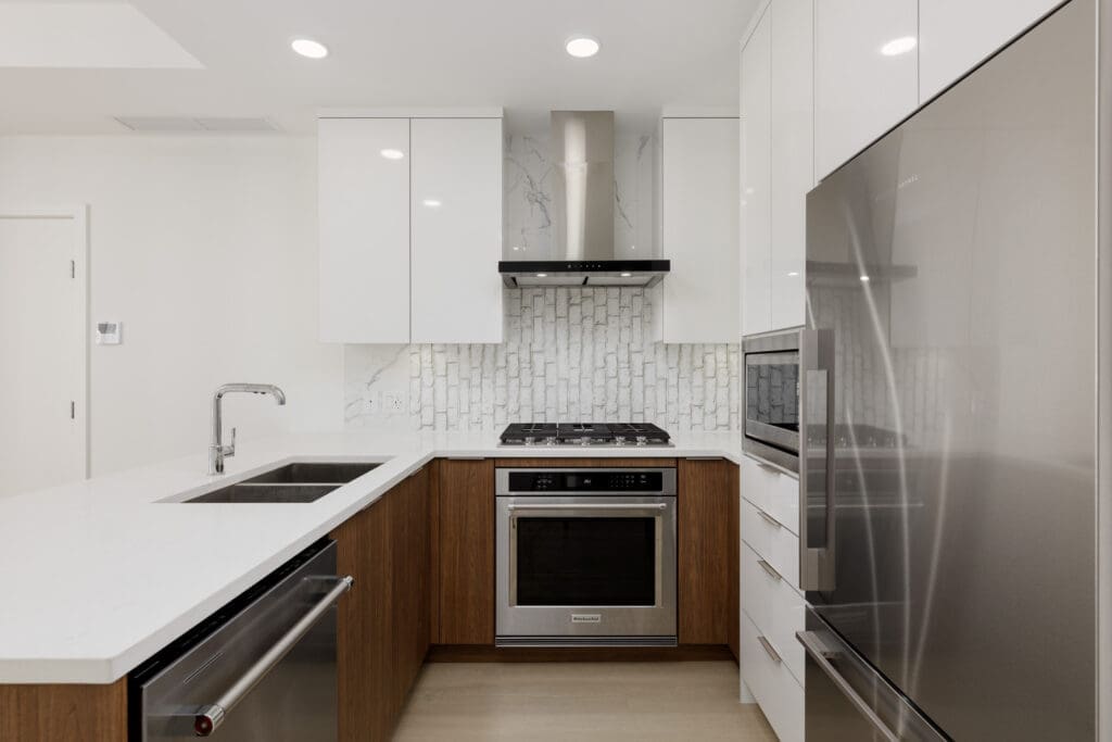 Modern kitchen with white cabinets, stainless steel appliances, a built-in oven, gas stove, double sink, and white tile backsplash.