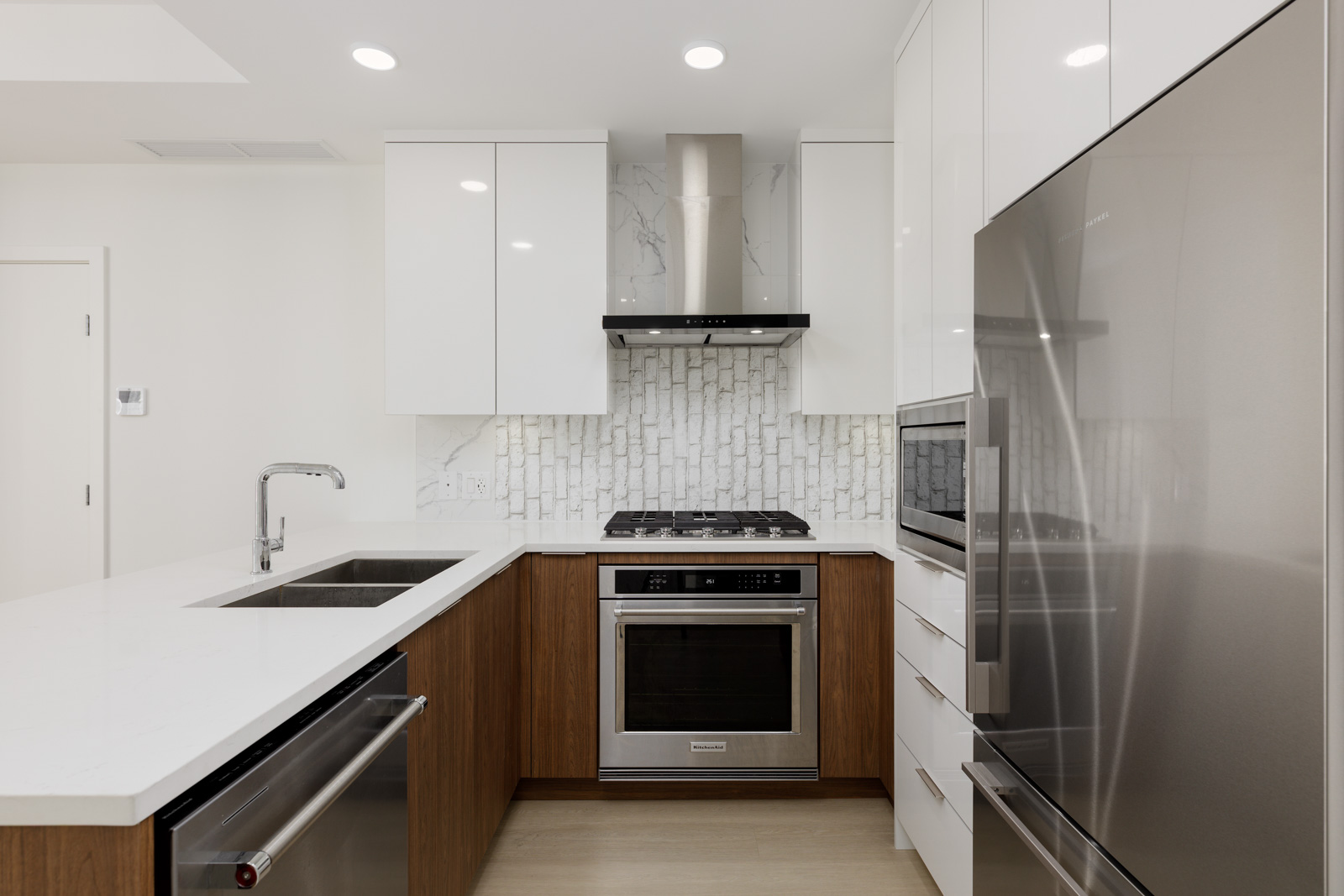 Modern kitchen with white cabinets, stainless steel appliances, a built-in oven, gas stove, double sink, and white tile backsplash.