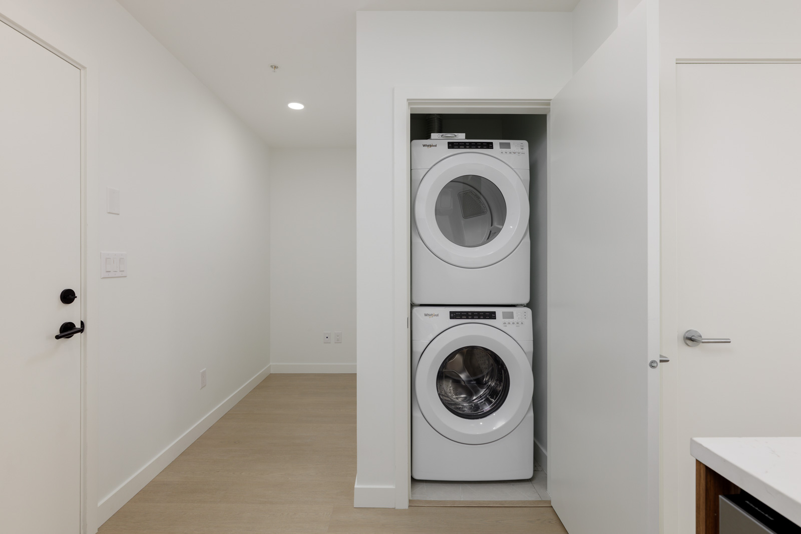 A stacked washer and dryer are installed in a small closet with a partially open door in a clean, modern laundry area.