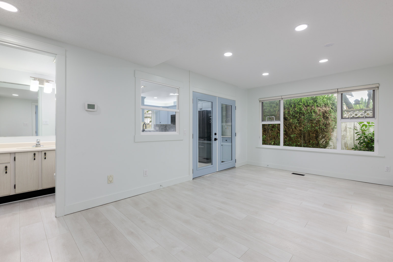 Unfurnished room with light-colored flooring, large window, glass door to outside, interior window, and view into an adjacent bathroom.