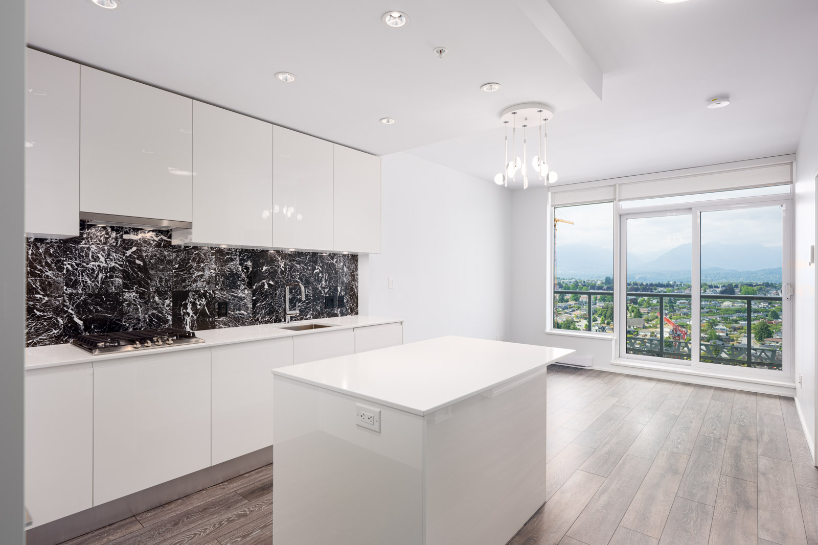 Modern kitchen with white cabinets, a black marble backsplash, island counter, wood flooring, and large windows overlooking a scenic view.