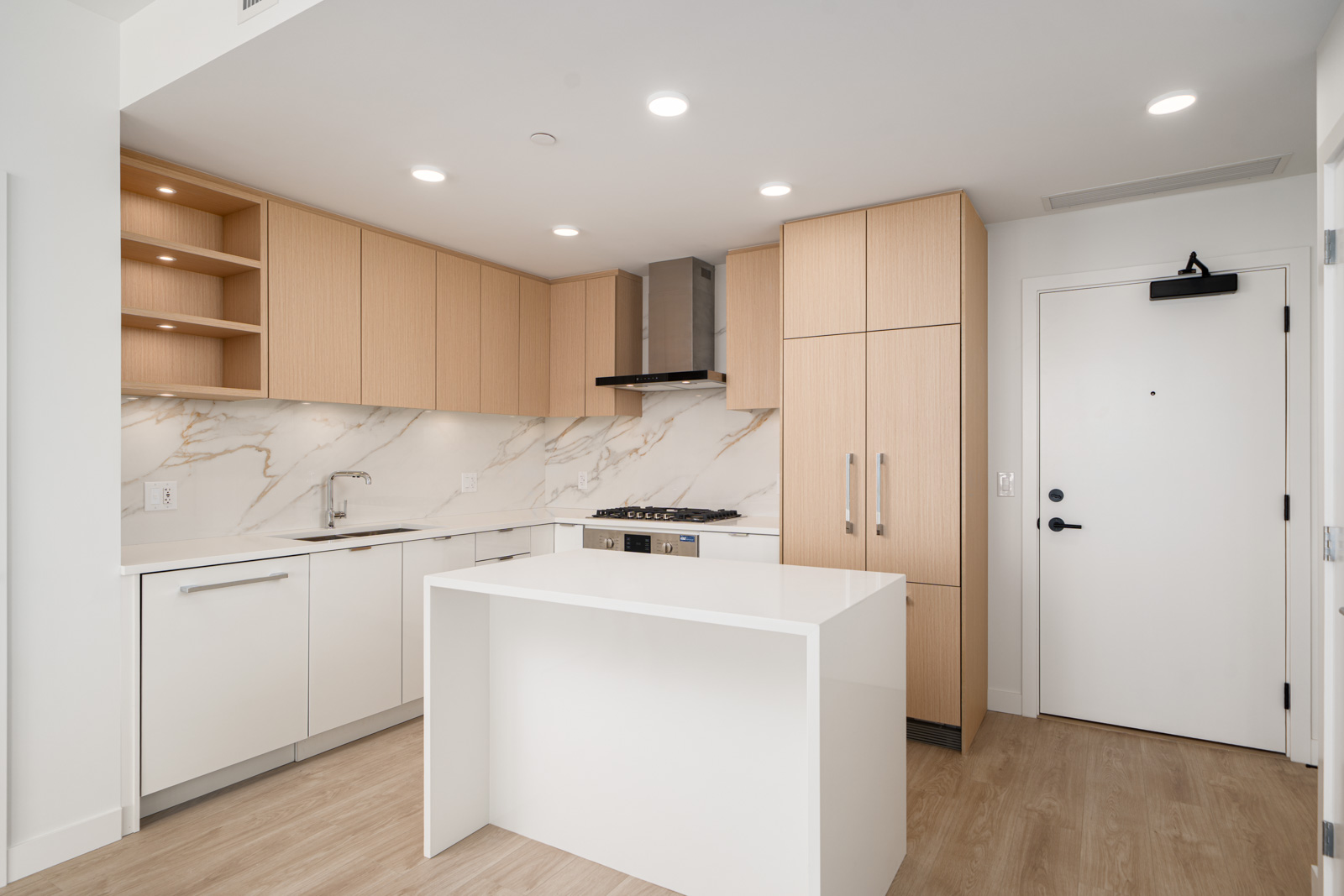Modern kitchen with light wood cabinets, white countertops, a marble backsplash, built-in appliances, an island, and recessed lighting.